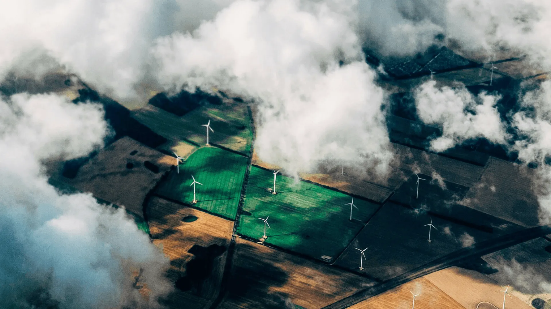 A high shot looking down, through the clouds at fields with windmills