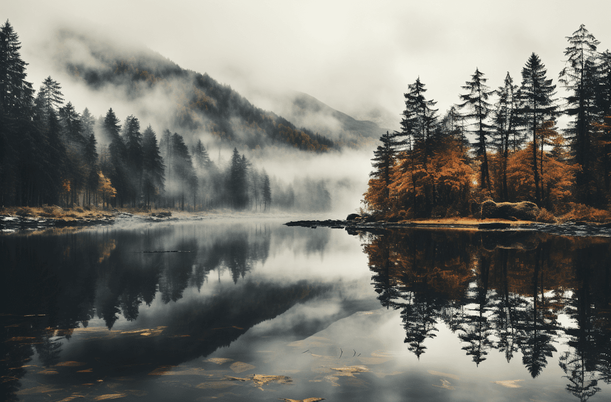 Scenic lake with misty mountains, autumn trees, and reflections on calm water in a natural setting.