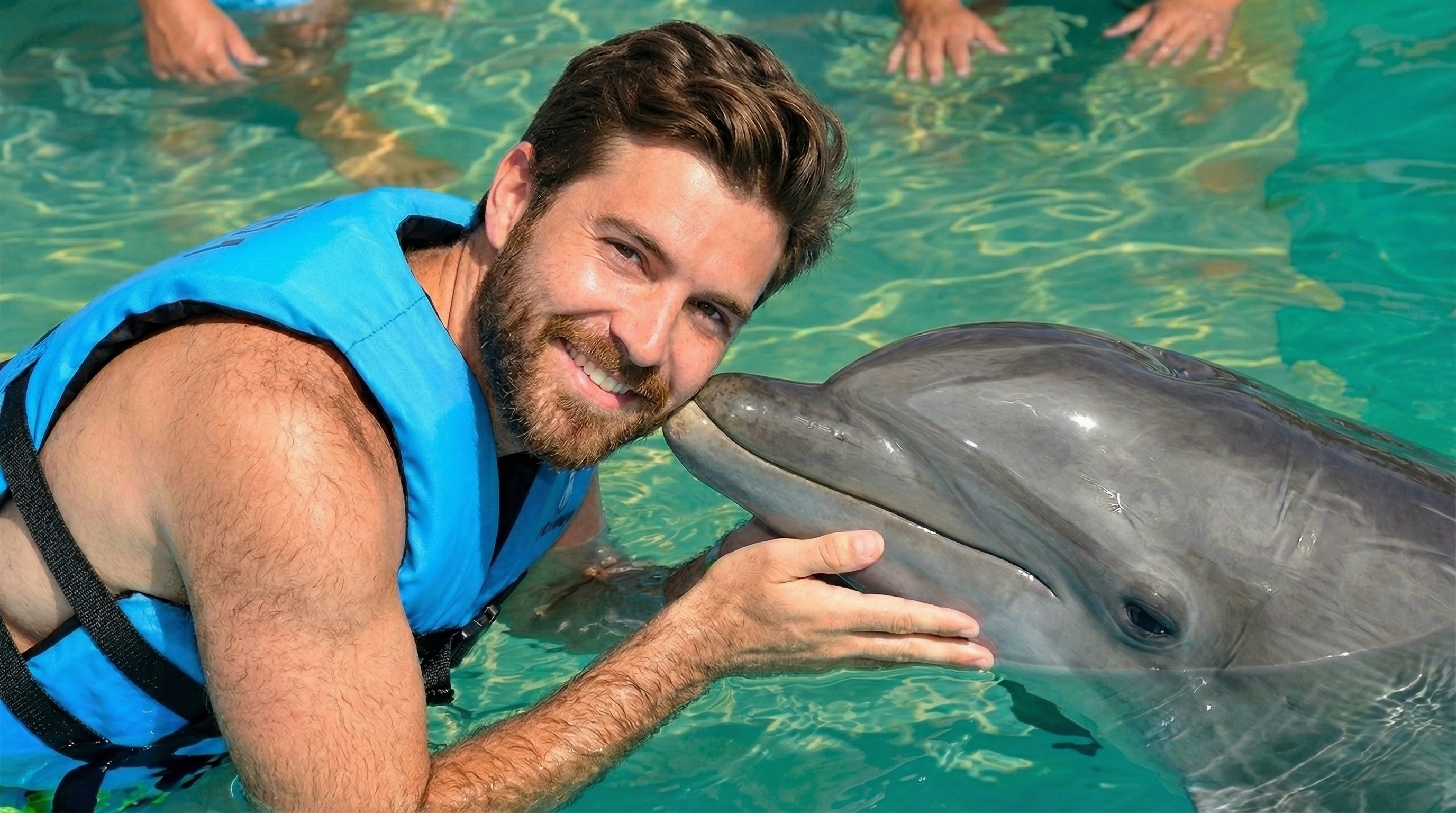 Smiling man in blue vest, nose-to-nose with a dolphin.