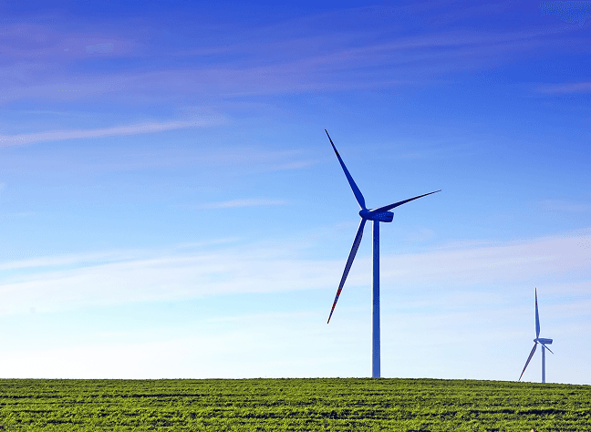 Wind turbines standing on a grassy field under a blue sky.