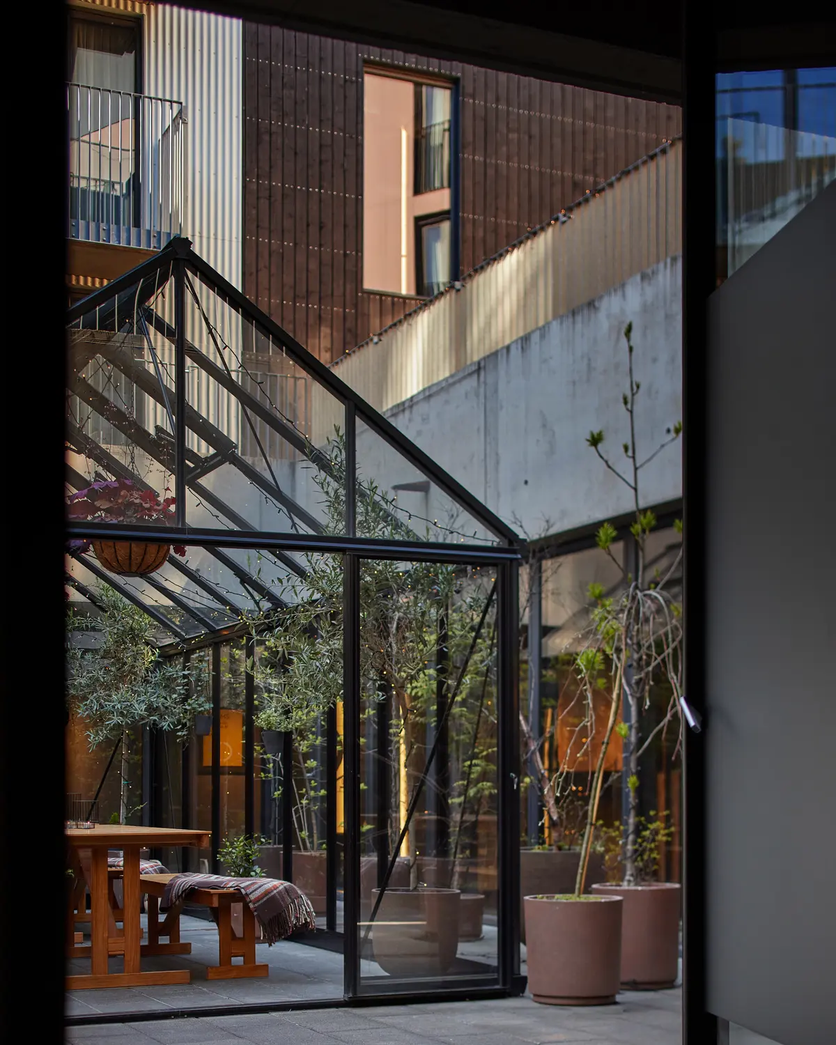 Glass garden house with potted plants and wooden tables in the hotel courtyard.