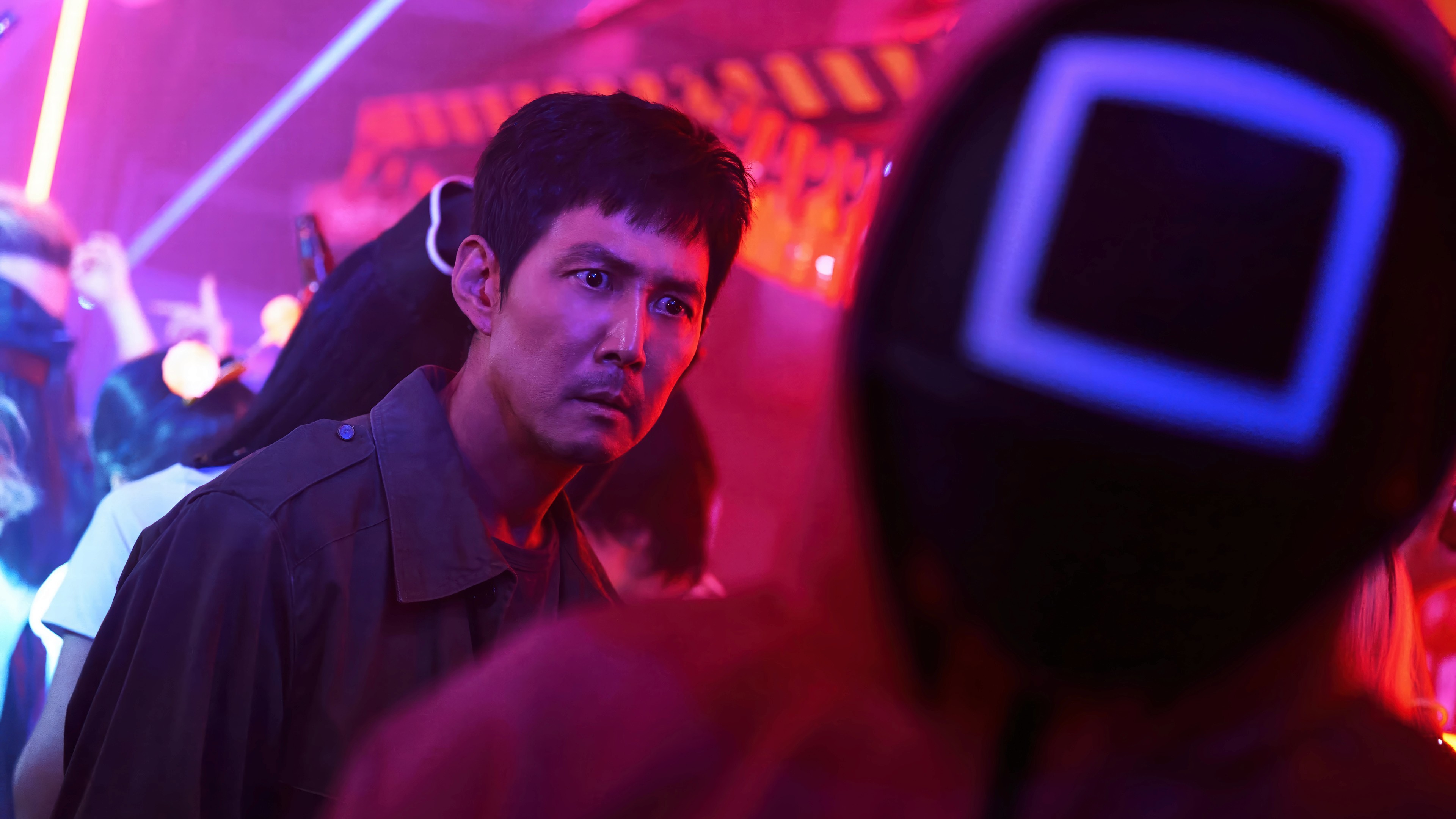 Lee Jung-jae as Seong Gi-hun in 'Squid Game', standing under neon lights with a tense expression.