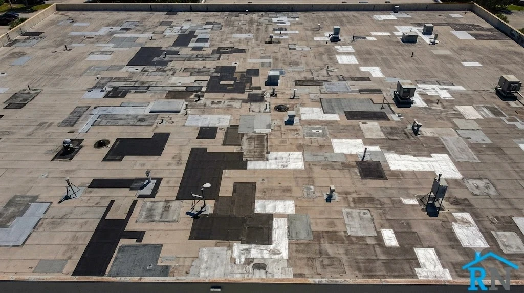 Aerial view of a large flat commercial roof in South Florida showing multiple patch repairs of different ages across the field