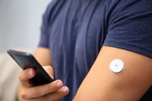 a person using a smartphone to check their glucose levels with a monitoring sensor attached to their upper arm, highlighting modern technology for continuous diabetes management