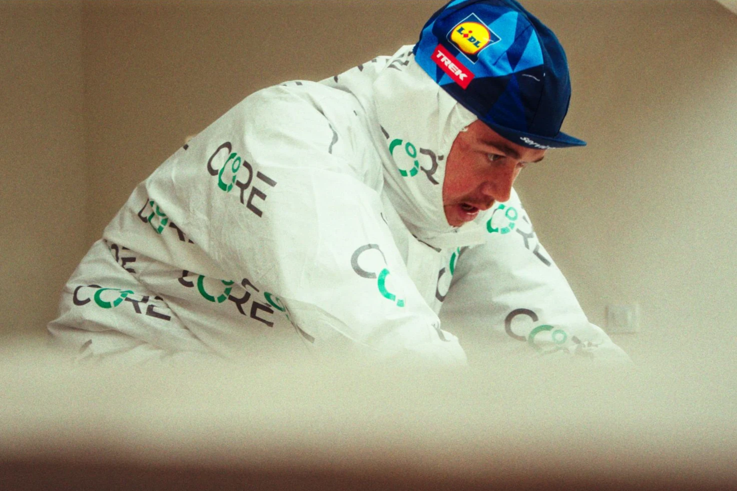 A Lidl-Trek rider on an indoor trainer in a white CORE heat suit and team cap, during a heat training session.