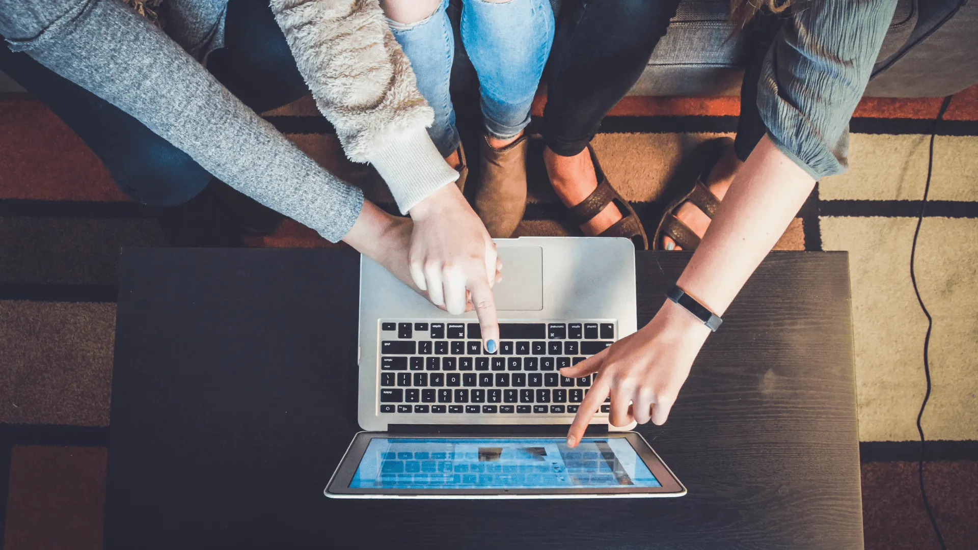 Three people sitting side by side all pointing at something on a screen of a laptop