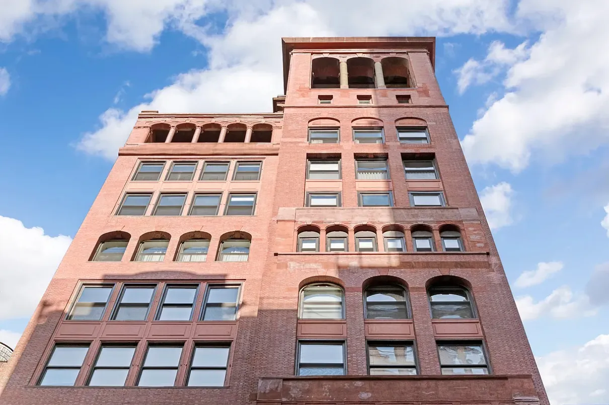A tall brick building featuring numerous windows and a prominent clock on its facade.
