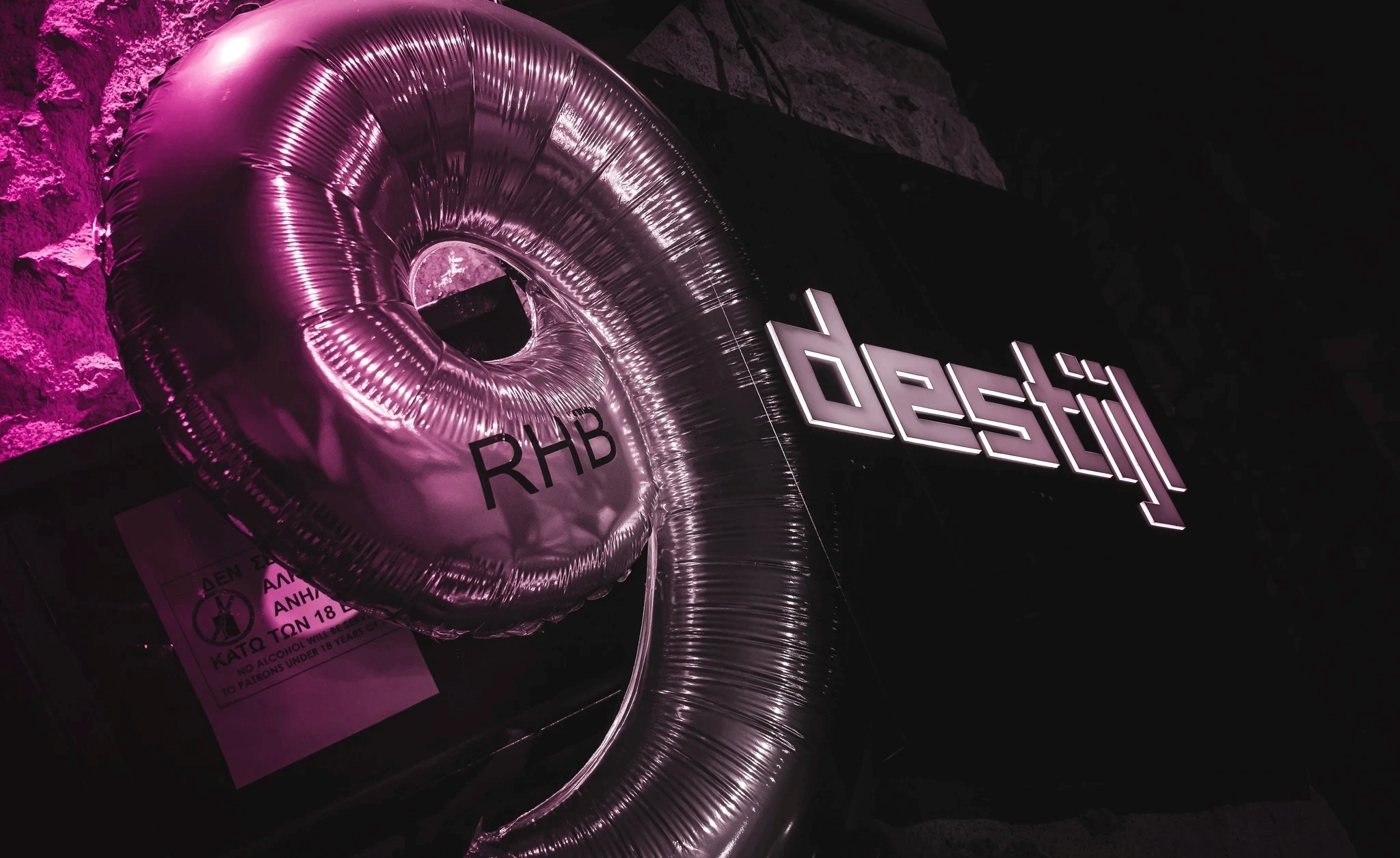A large, plastic pink number '9' balloon with "RHB" printed on it hangs in a club next to a lit-up sign for "destijl".