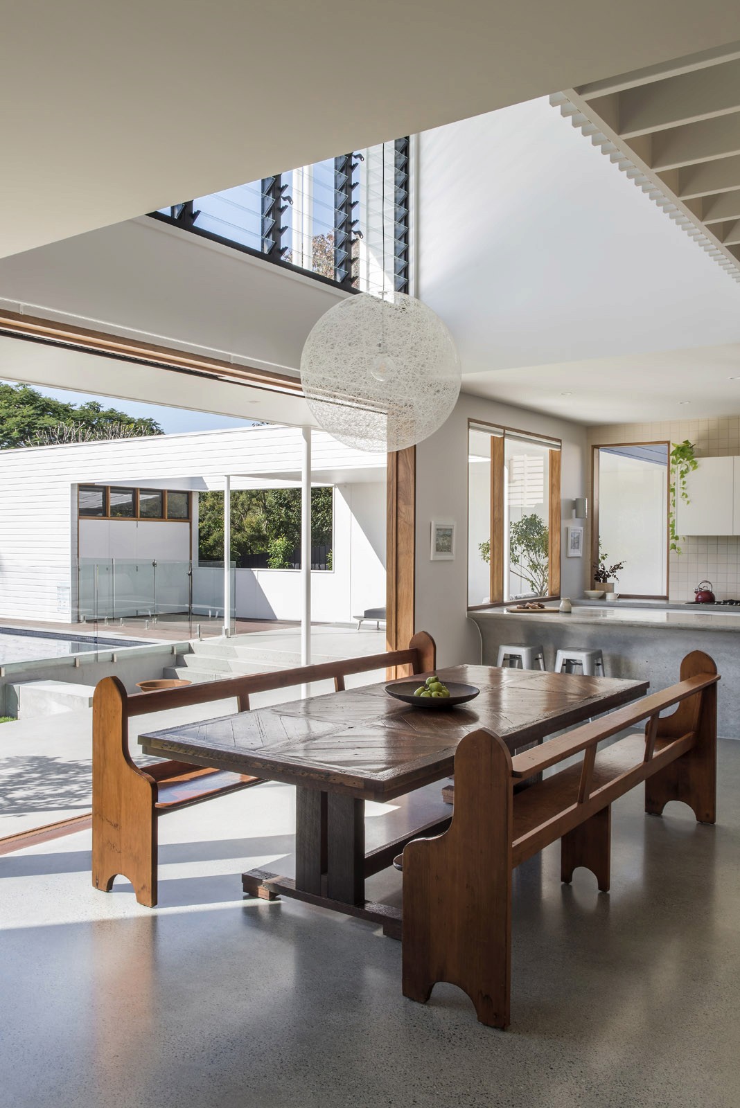 Interior dining area with timber table, skylight, and open connection to outdoor pool and courtyard