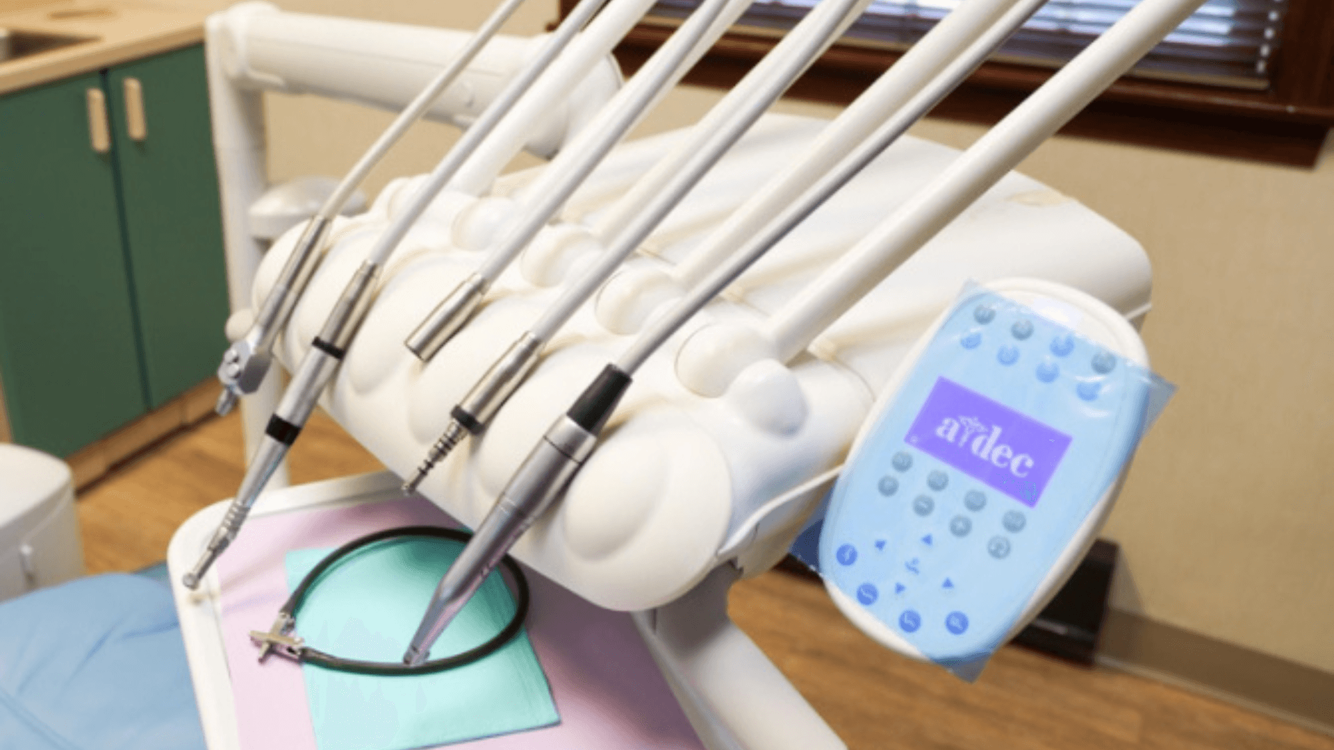 Alt tag: Close-up of dental equipment with multiple handpieces attached to a dental chair unit, including a control panel, in a clinical exam room.