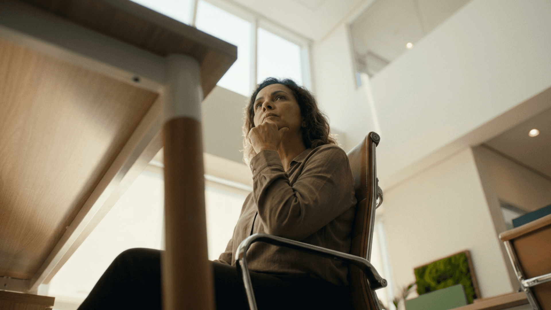 Gestora de clínica sentada em poltrona de couro, com a mão no queixo e o olhar pensativo voltado para cima, refletindo sobre decisões sem indicadores. Imagem da Tivita para conteúdo sobre gestão de clínicas por dados.