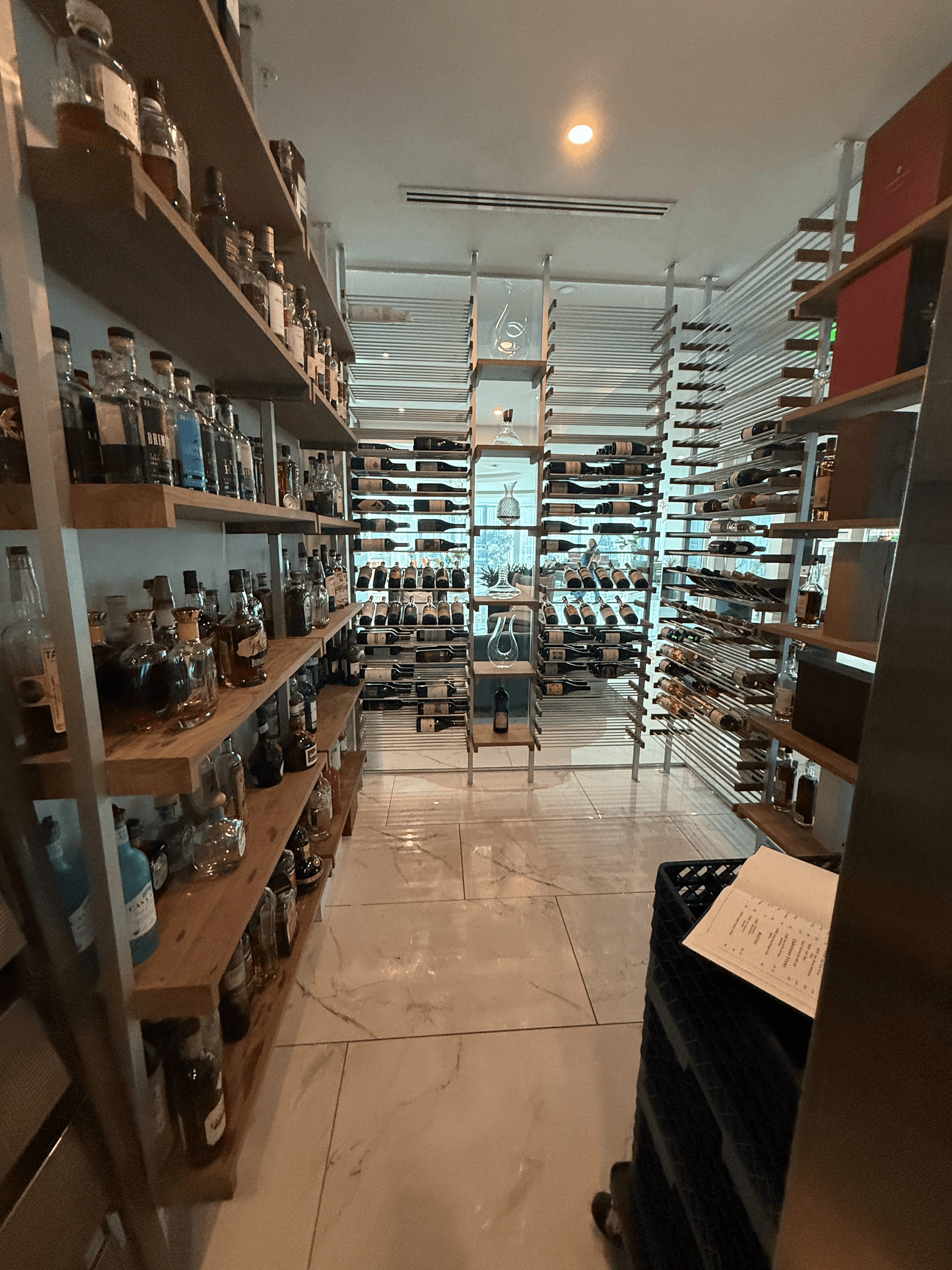Interior view of the Cambria Waco Hotel wine cellar featuring aluminum and walnut wine racks, wood shelving for spirits, and climate-controlled storage designed by Prestige Wine Cellars.