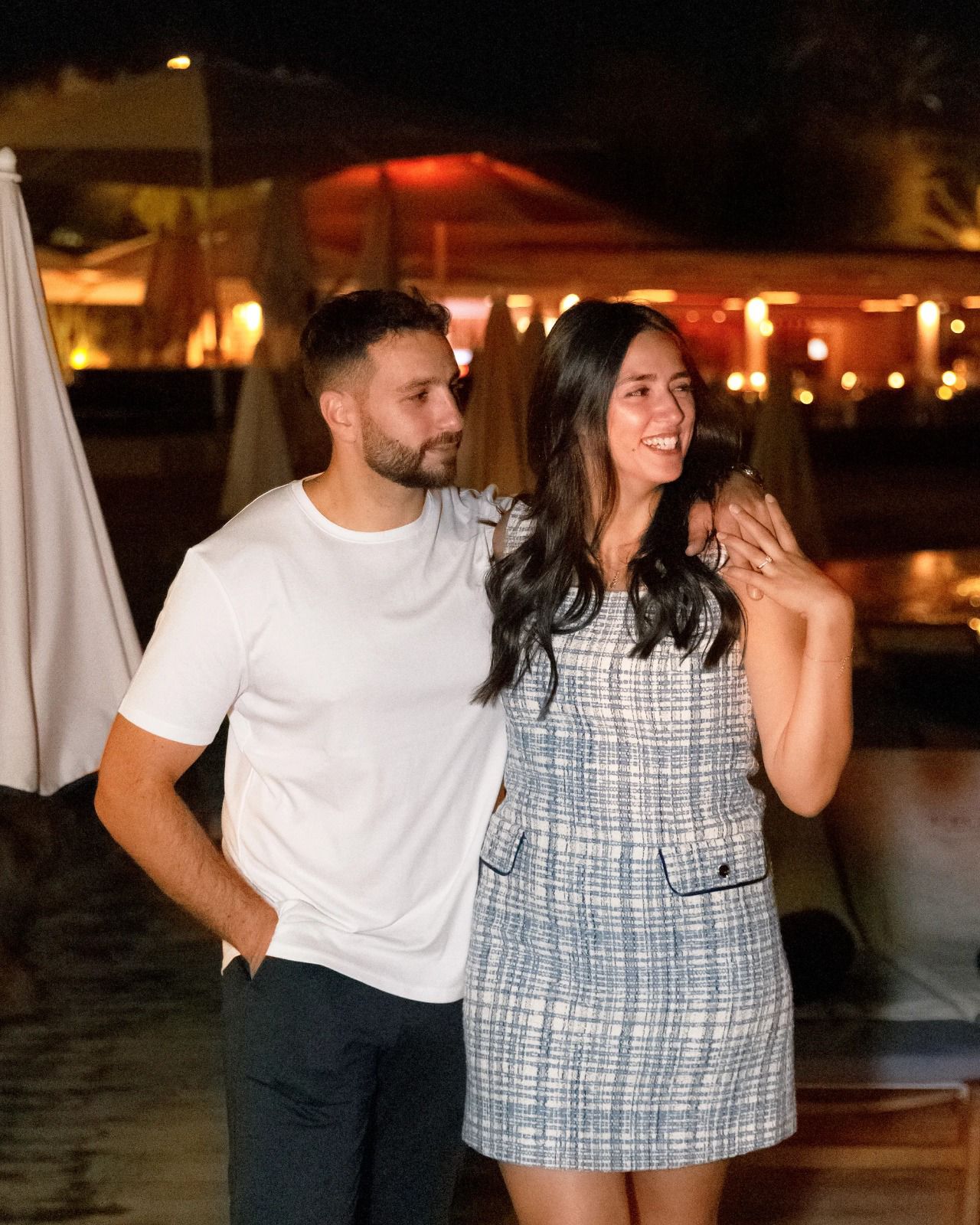 A woman with long blonde hair, in a brown top and jeans, walks through a sunlit forest, holding someone's hand. The scene is warm and inviting.