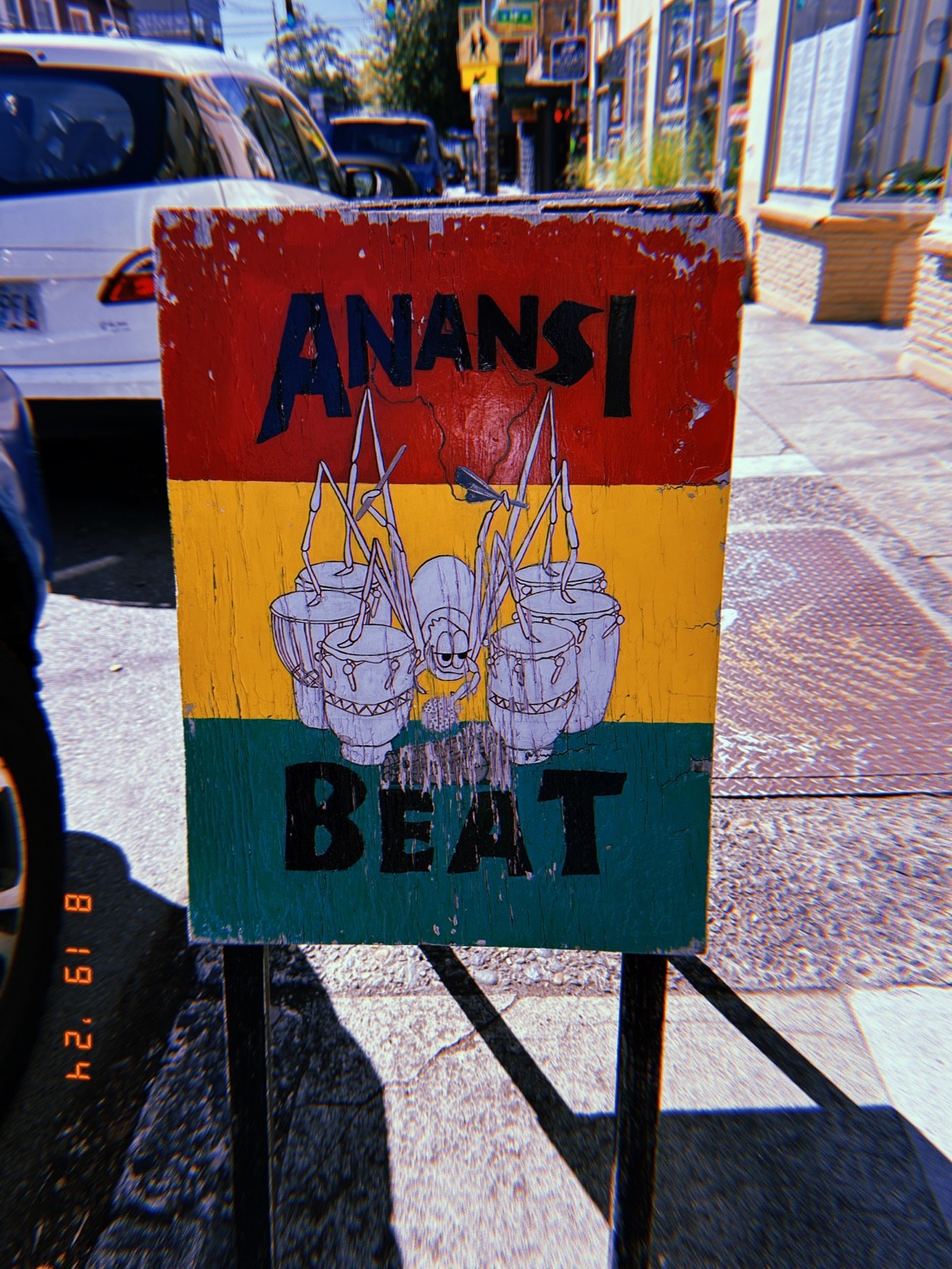 A painted Anansi & the Beat pavement sign, photographed in context. Photograph by Pranjali Shah.