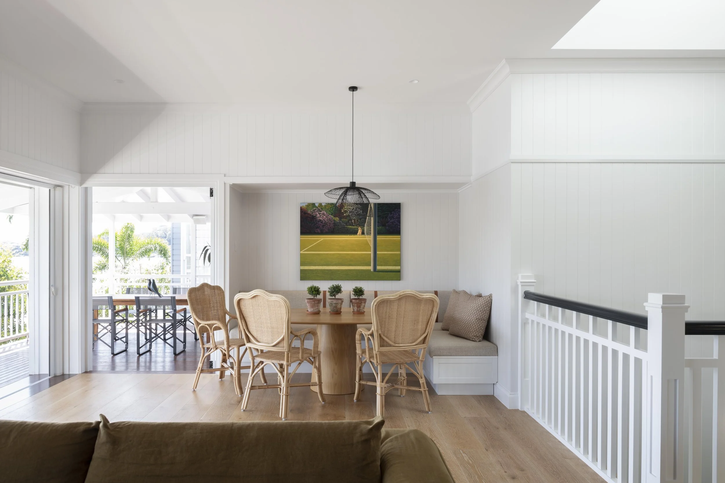 Open-plan dining area with rattan chairs, pendant light, and connection to outdoor deck.