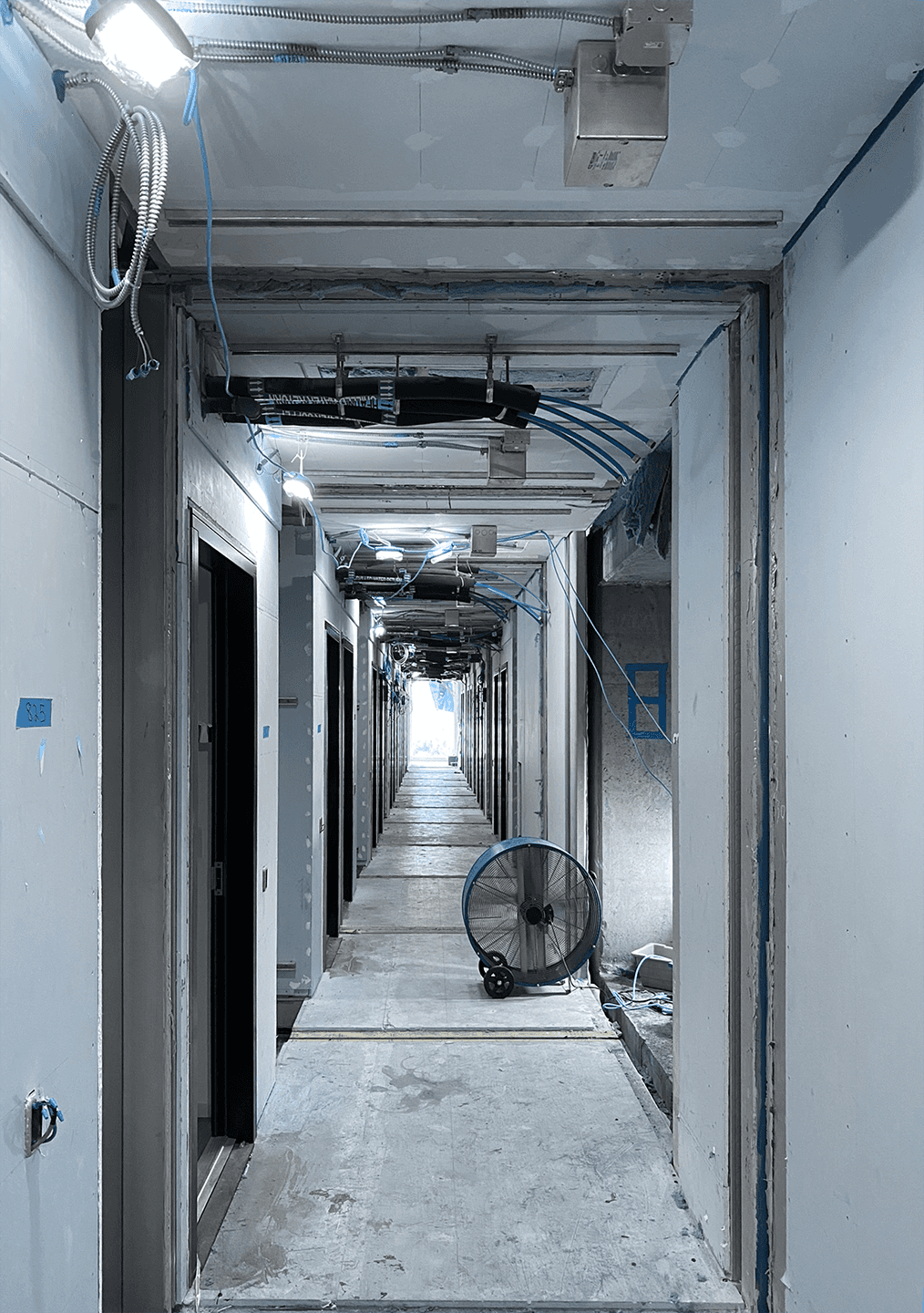 Guestroom hallway under construction with exposed wires and visible room-to room joints, highlighting modular system tolerances.