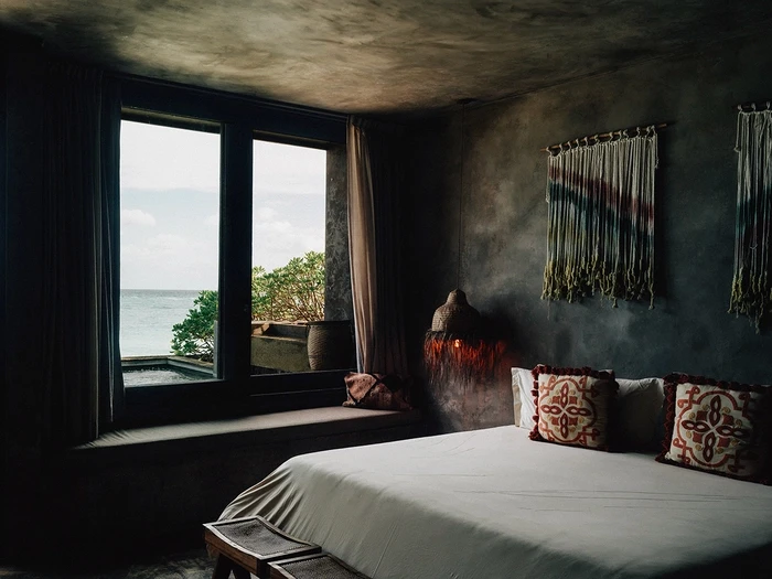 Premier Suite at Nômade Tulum highlighting part of the bed with pillow and cushion, and bright and beautiful lamp next to the bed.