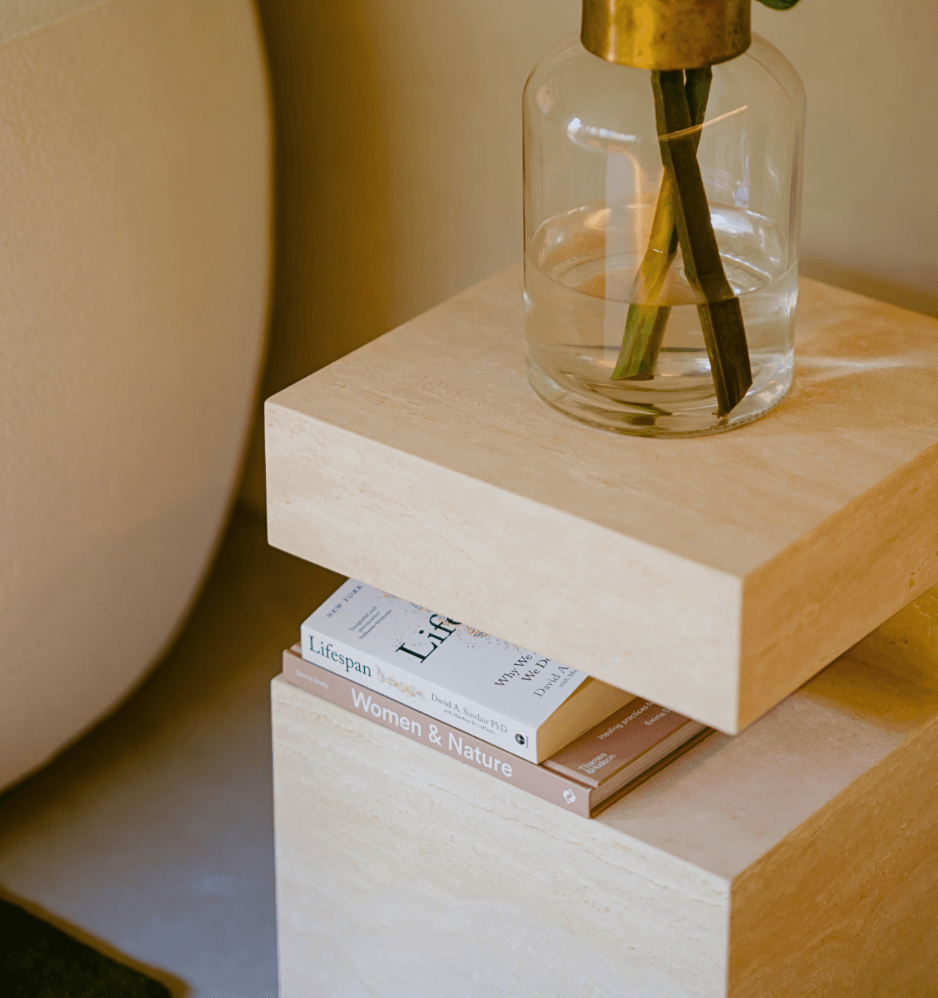 A plant in a transparent vase placed on a small coffee table, with books stacked underneath it.