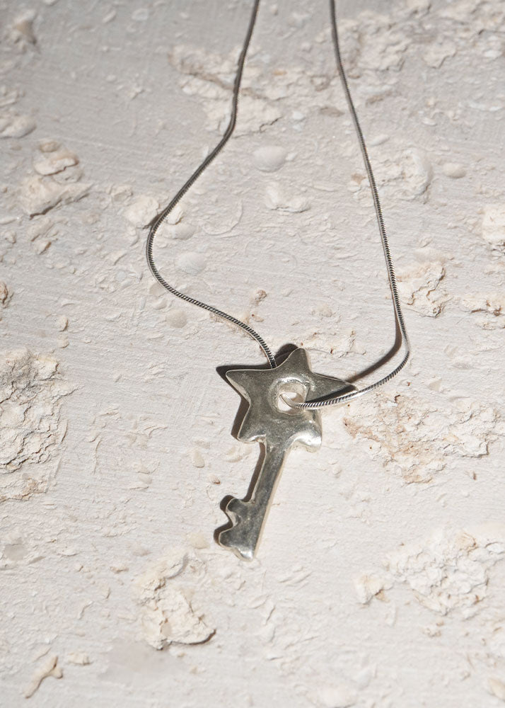 Silver key-shaped pendant on a chain against a textured light gray background