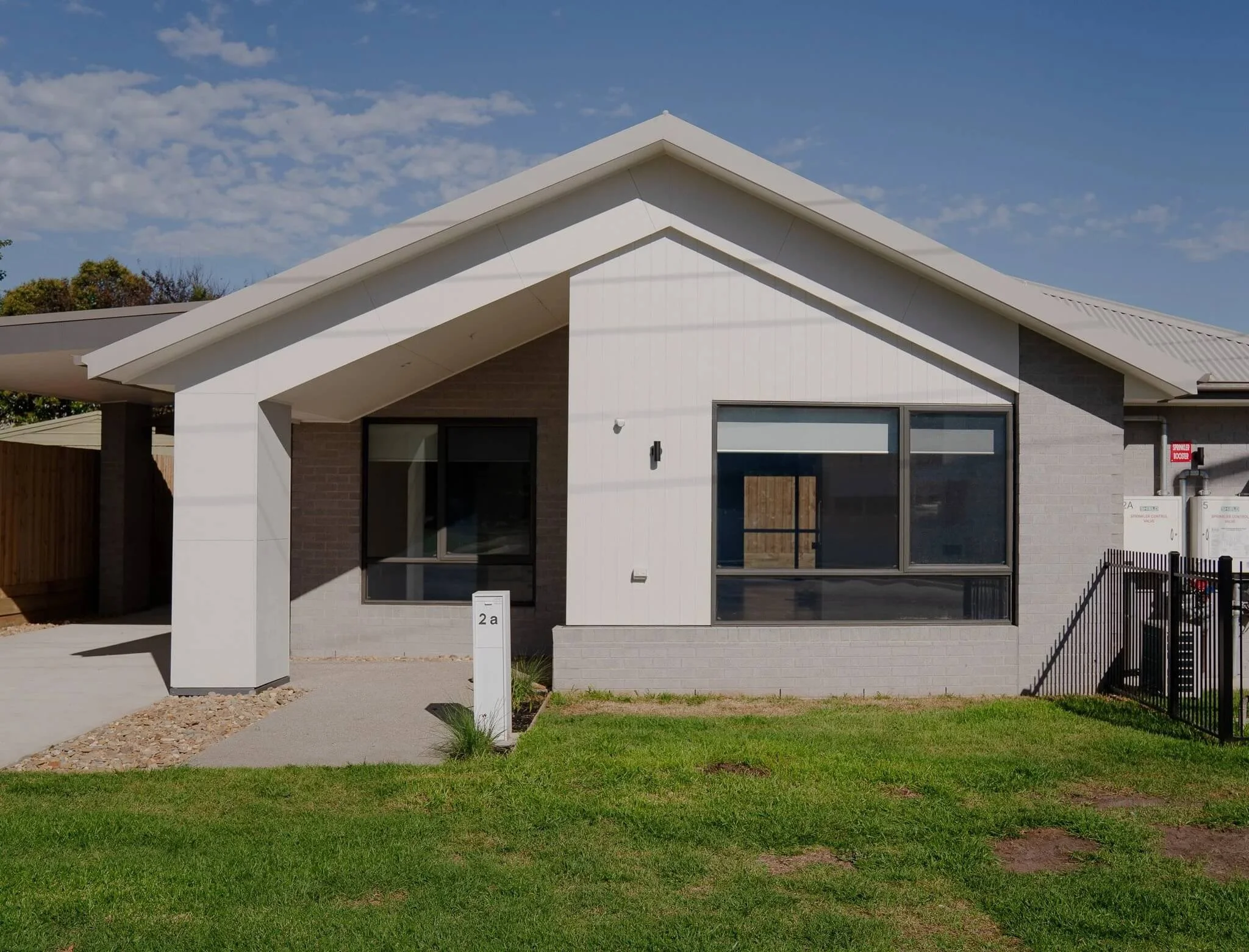 Modern single-story house with a gray brick exterior, large front window, and well-maintained lawn.