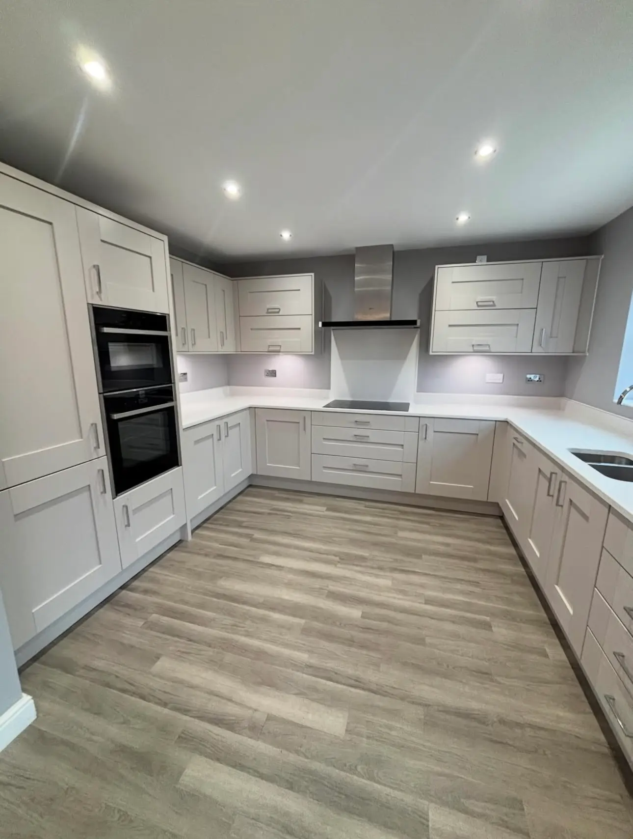 A spacious, empty kitchen after a professional move-out clean, featuring spotless white cabinetry, polished countertops, and a vacuumed wood-plank floor.