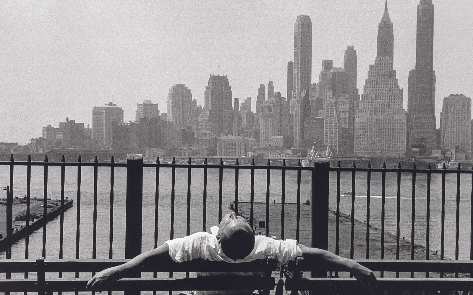 Persona recostada en un banco con vista al horizonte de la ciudad al otro lado del agua.