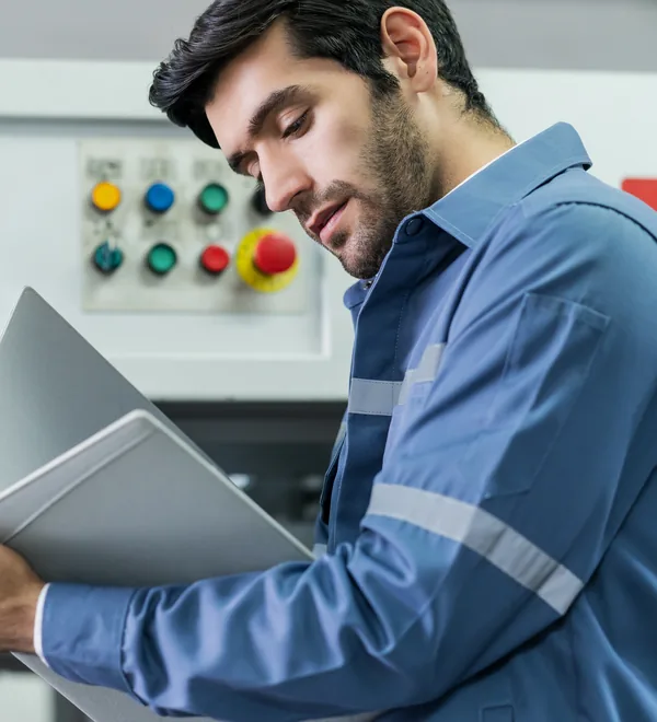 Engineer with a laptop checking readings at a machine control panel in a factory