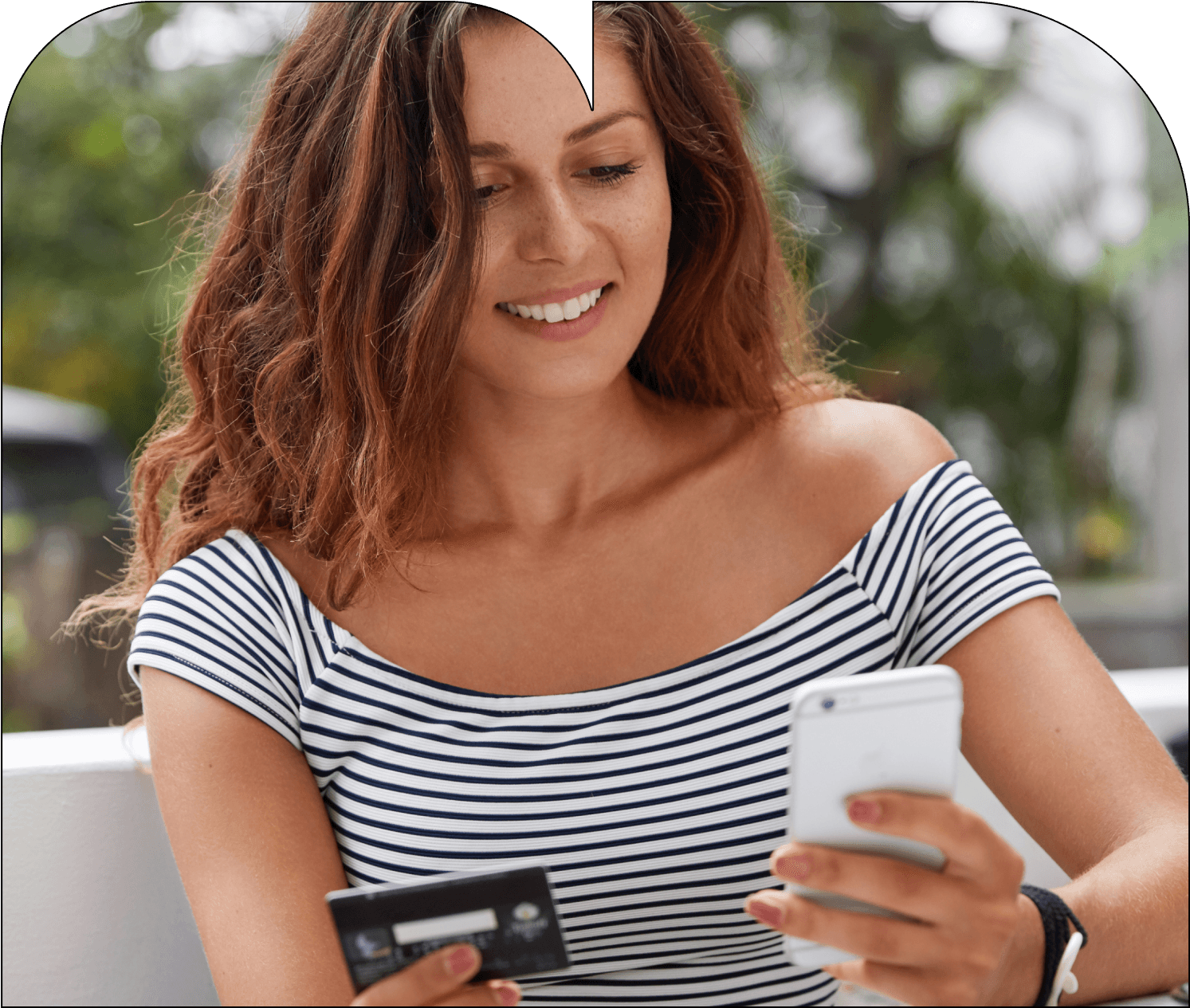 A young woman with long brown hair is sitting outside in a relaxed setting, holding a credit card in one hand and a smartphone in the other. She is smiling while making a purchase. A green icon displaying "Installments 3/4" overlays the image, indicating that she is using Breezy’s installment payment option.