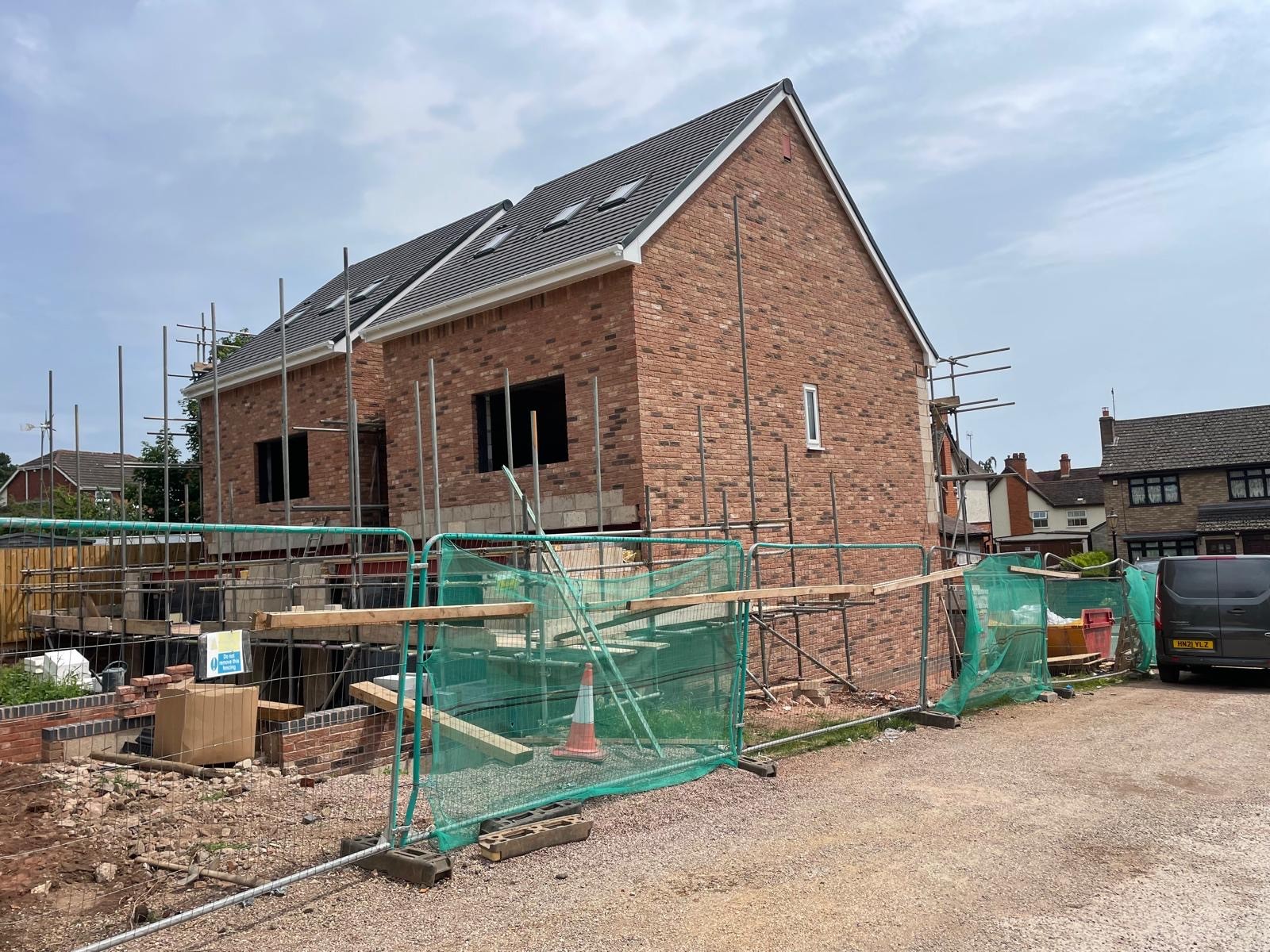 A partially constructed house with exposed brick and scaffolding, surrounded by construction materials and debris.