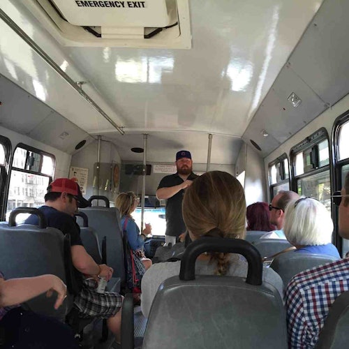 乘客坐在公車上，而一名穿著黑色襯衫和藍色帽子的鬍鬚男子正站在前面講話。