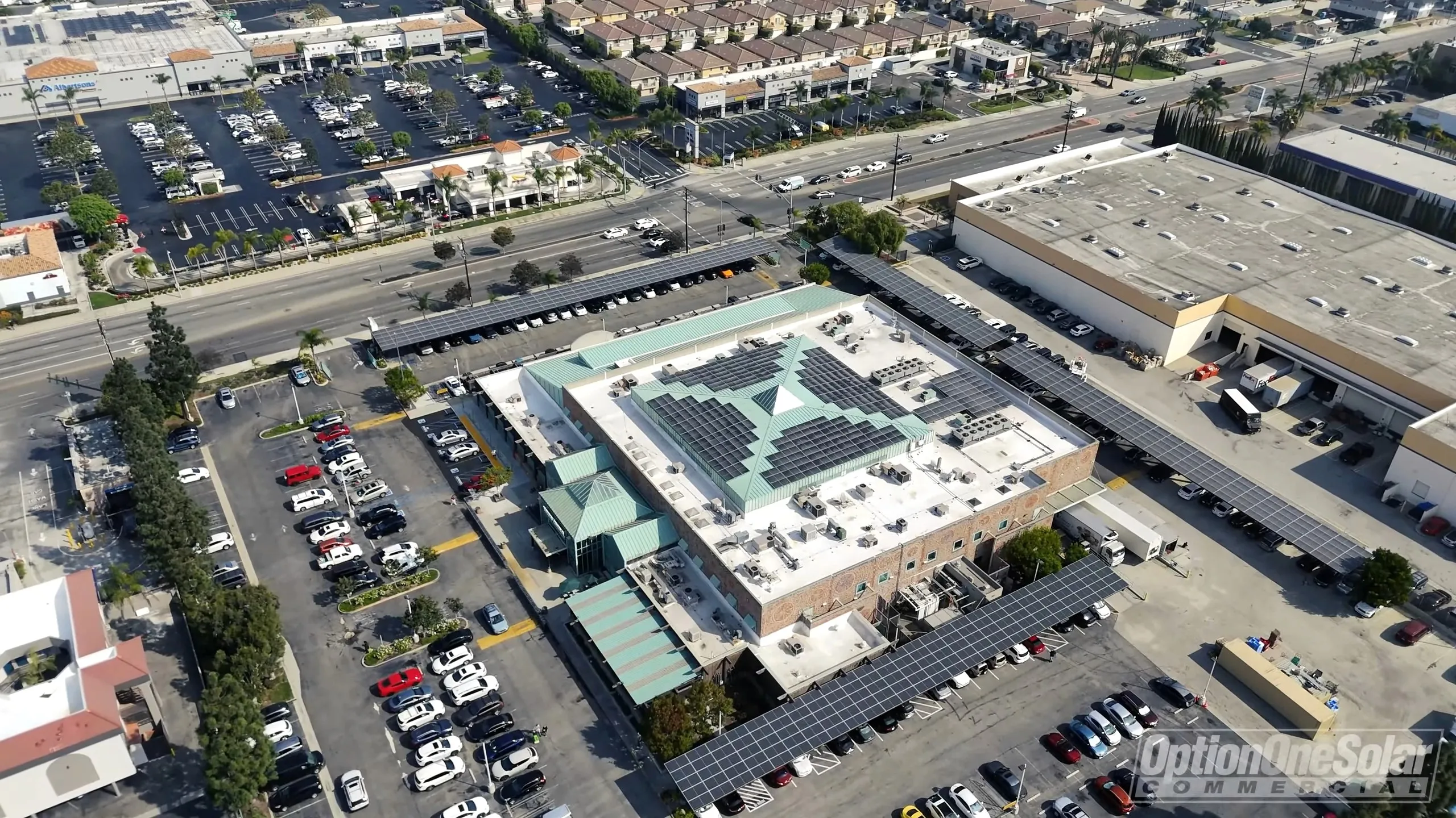 Aerial view of a shopping center with rooftop solar panels and solar carports over the parking lot