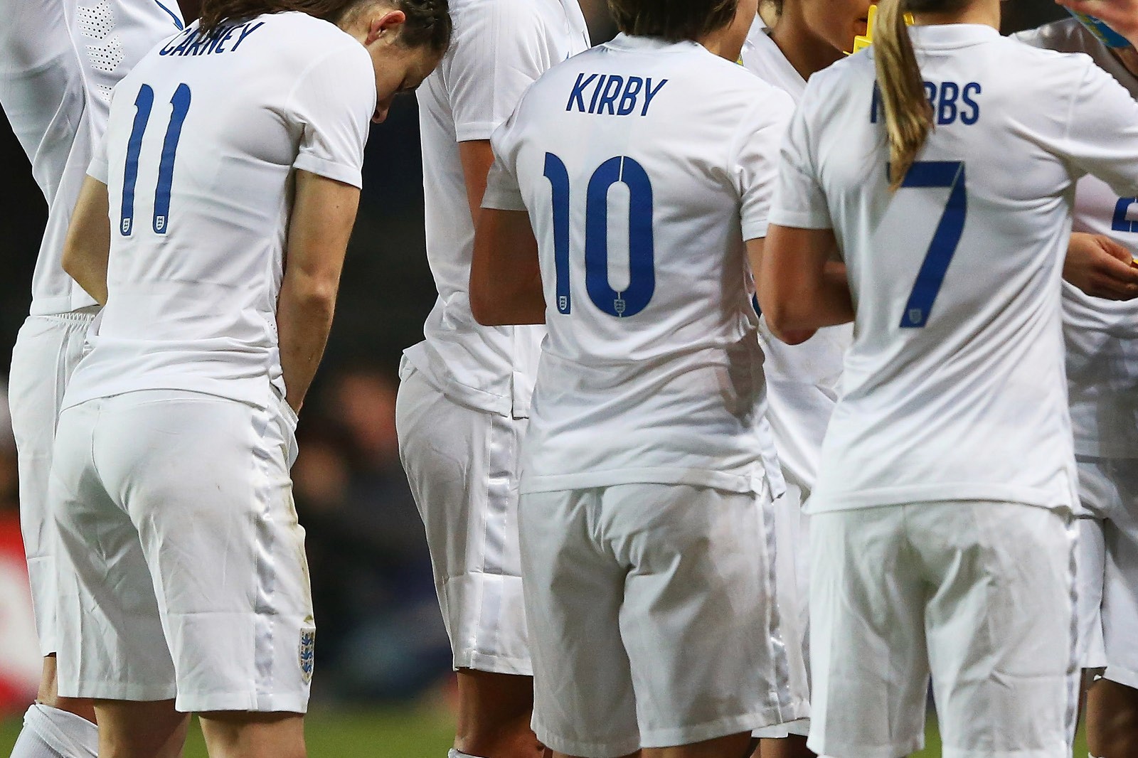 A group of players (England Lionessess) in white jerseys, numbered 7, 10, and 11, huddled together on the field.