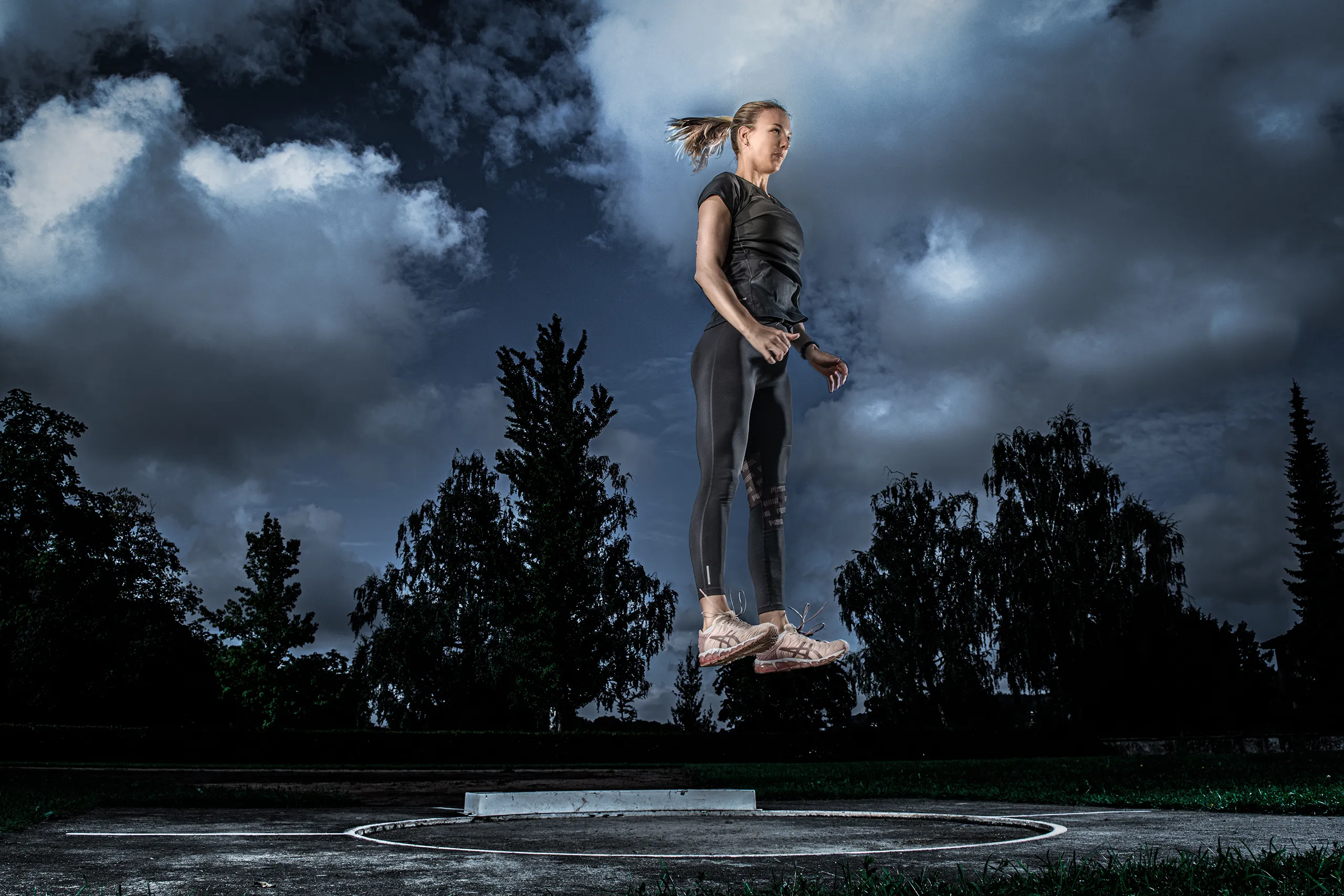 Action shot of a female athlete suspended in mid air during a long jump against a dramatic cloudy background.