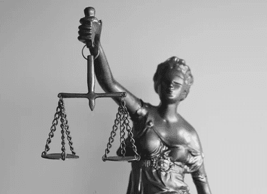 Uma imagem em escala de cinza de uma estátua da Senhora Justiça segurando uma balança equilibrada, simbolizando imparcialidade e justiça.