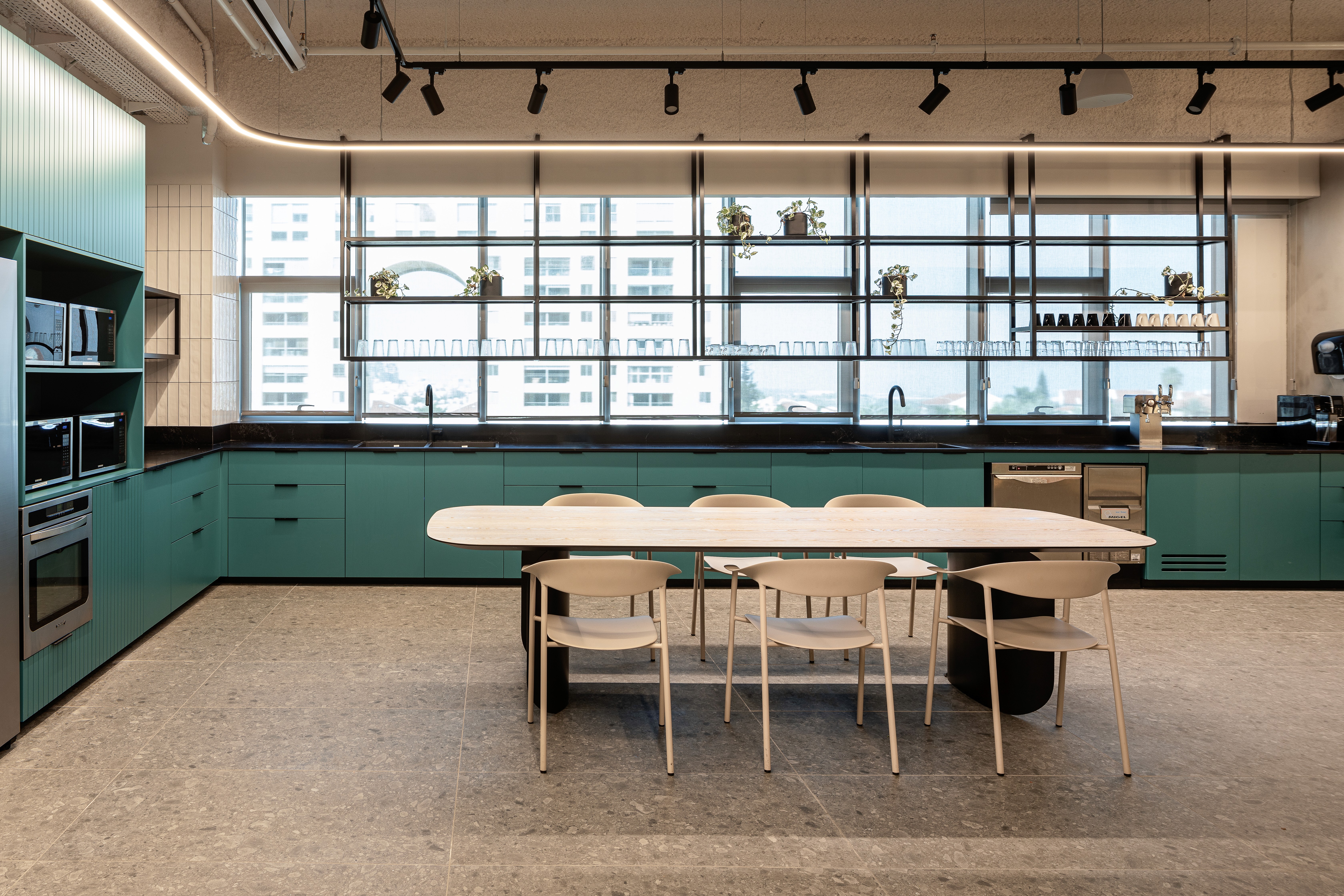 מטבח וקפיטריה: עיצוב בסגנון בית קפה עם חיפוי אריחים ירוקים, נגרות בהירה ושולחנות משותפים לעידוד אינטראקציה חברתית בין העובדים.