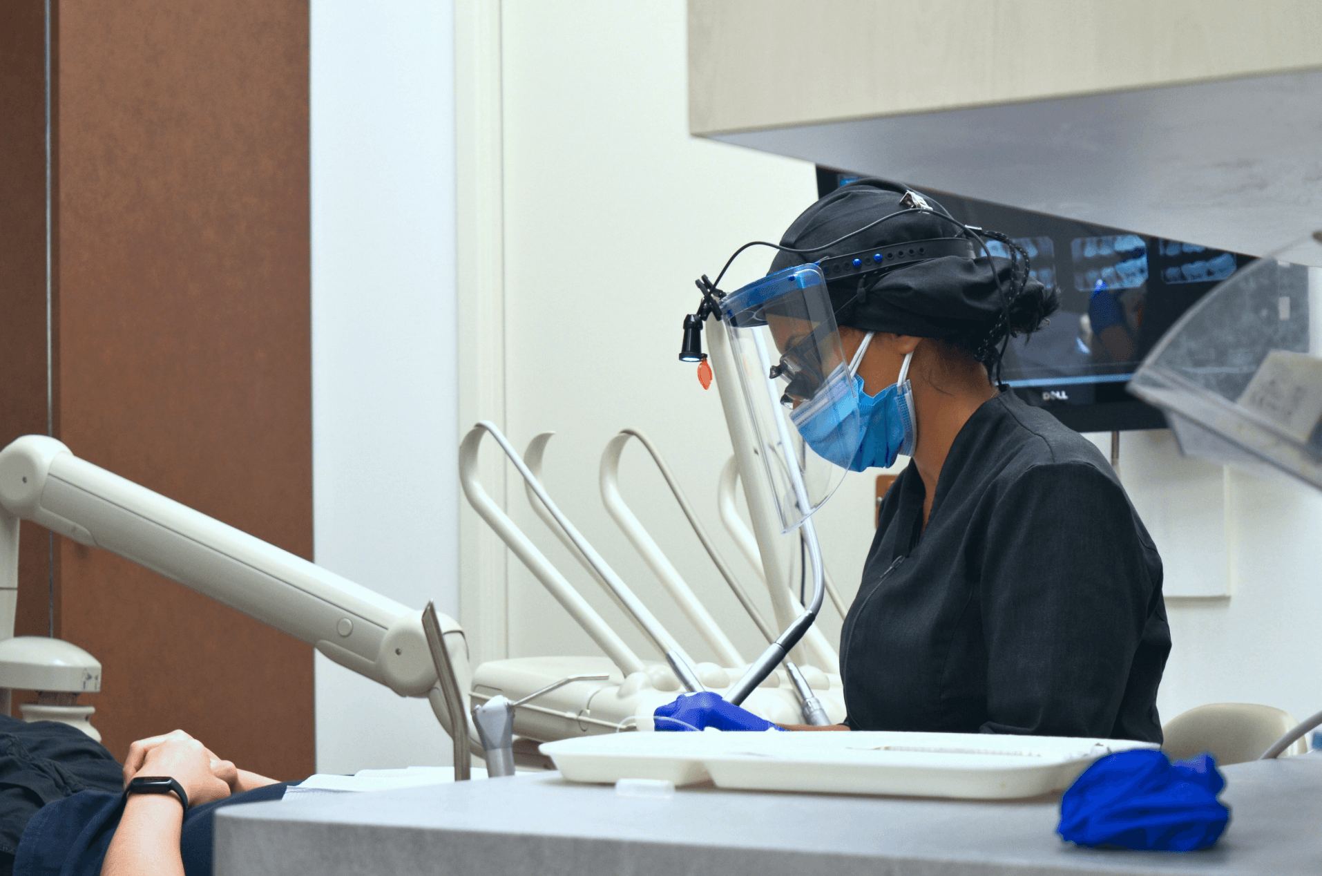 A dental professional wearing a face shield and mask working on a patient's teeth in a dental clinic.