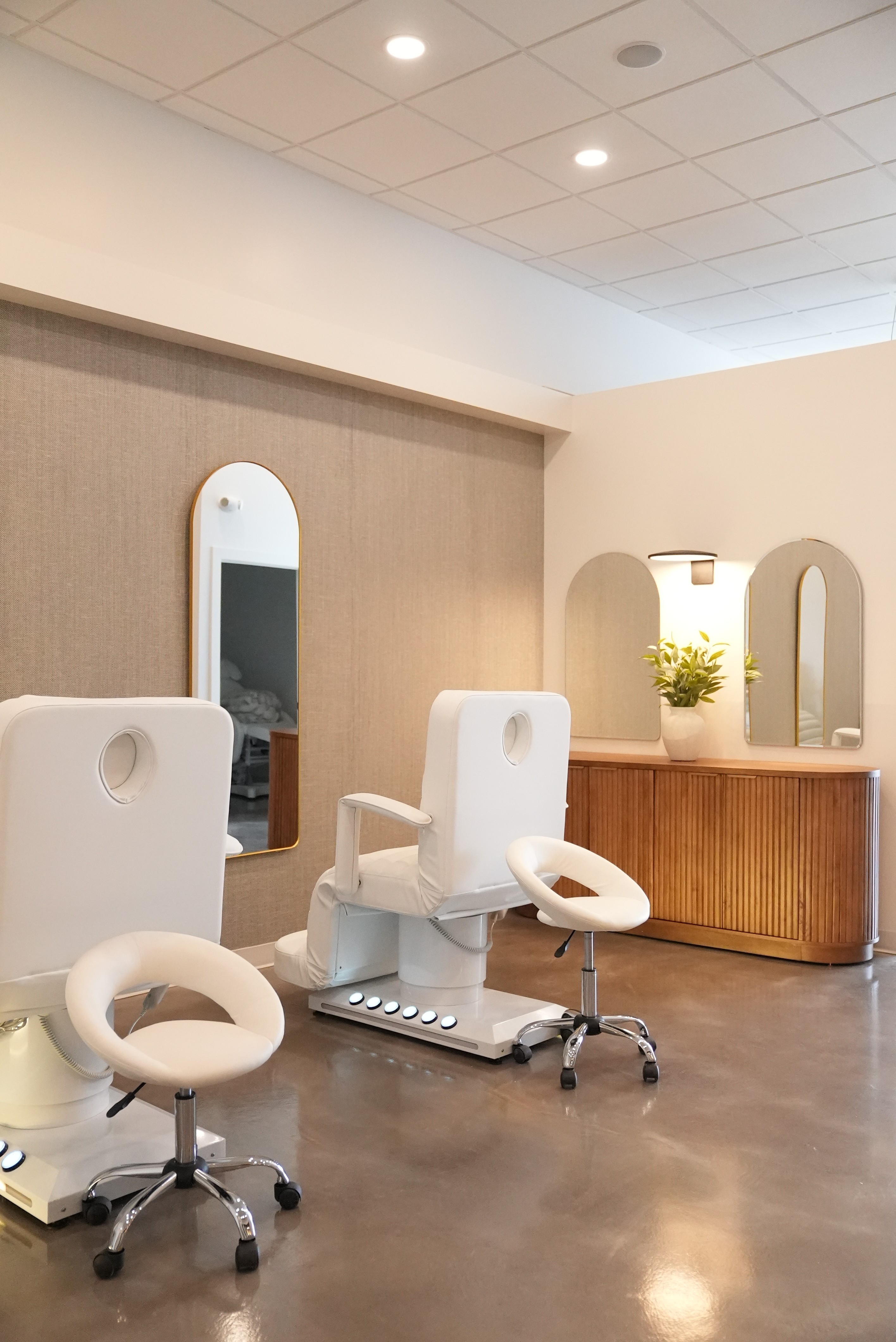 A serene and elegant spa space with wooden reclining chairs and white cushions. Golden sunlight filters through a cascading water feature, creating a peaceful atmosphere. Tropical plants and candles add to the relaxing ambiance.