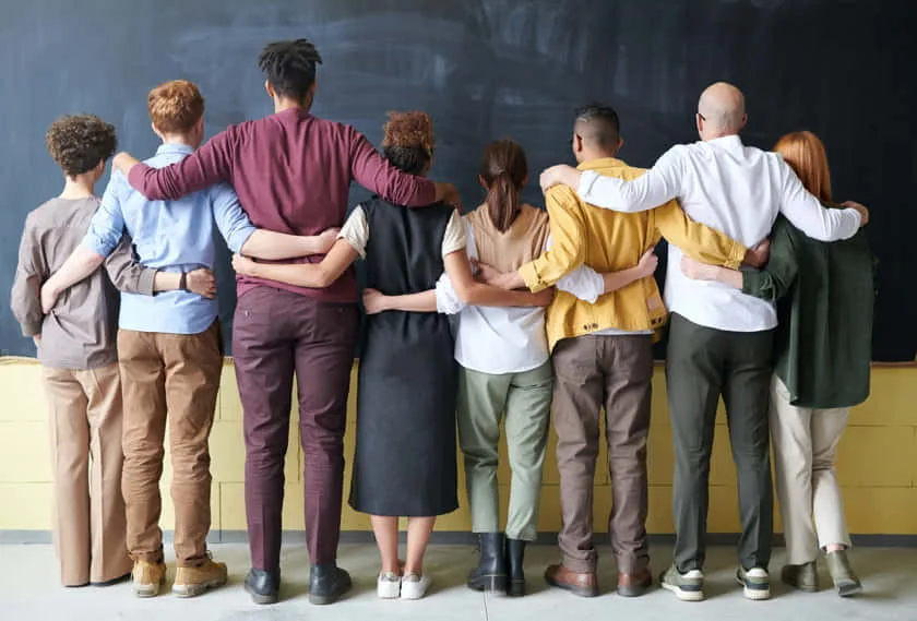 Group of diverse people standing side by side with arms around each other, showing unity and Community.