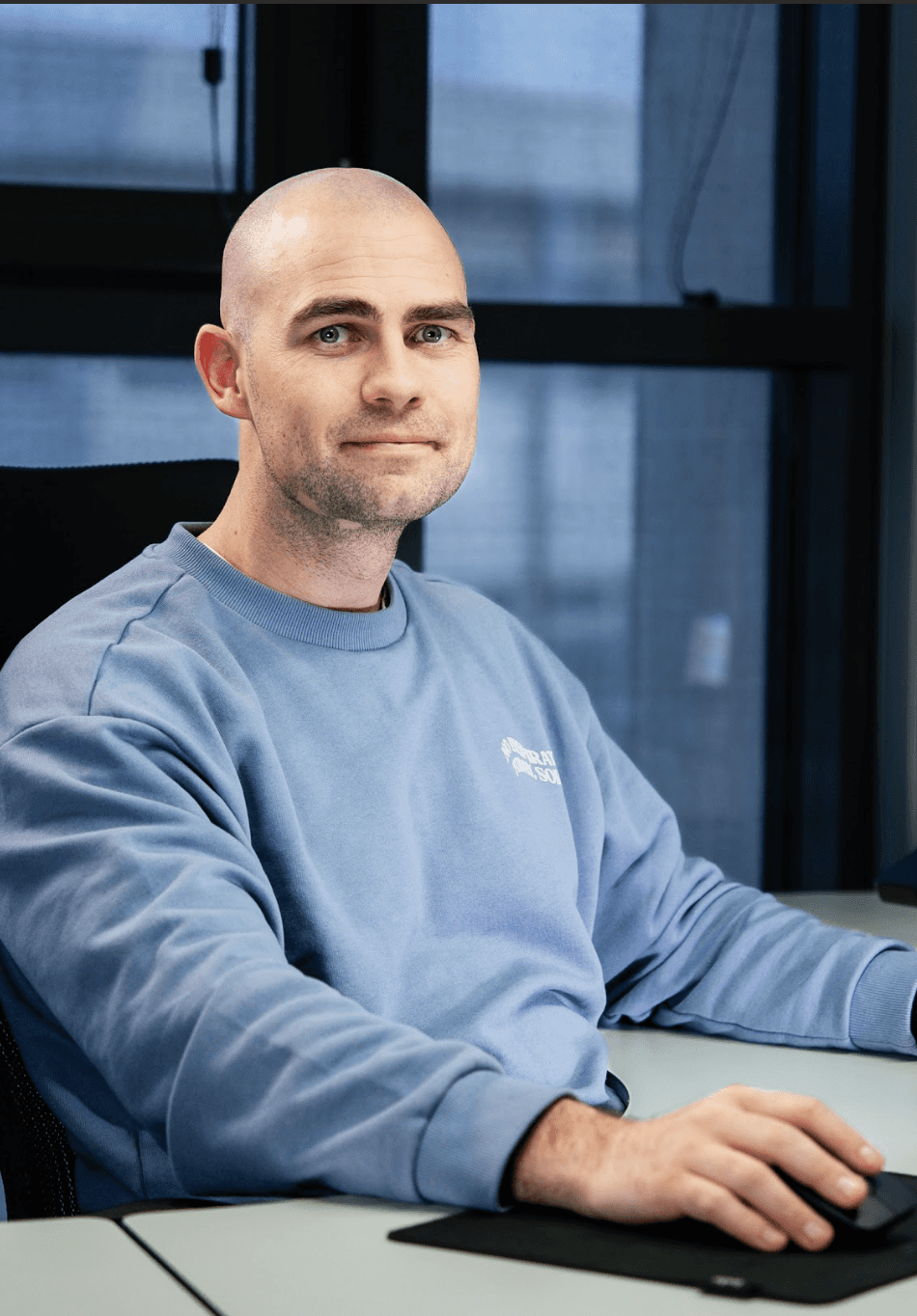 Smiling woman with curly hair and glasses using a smartphone in an office setting.
