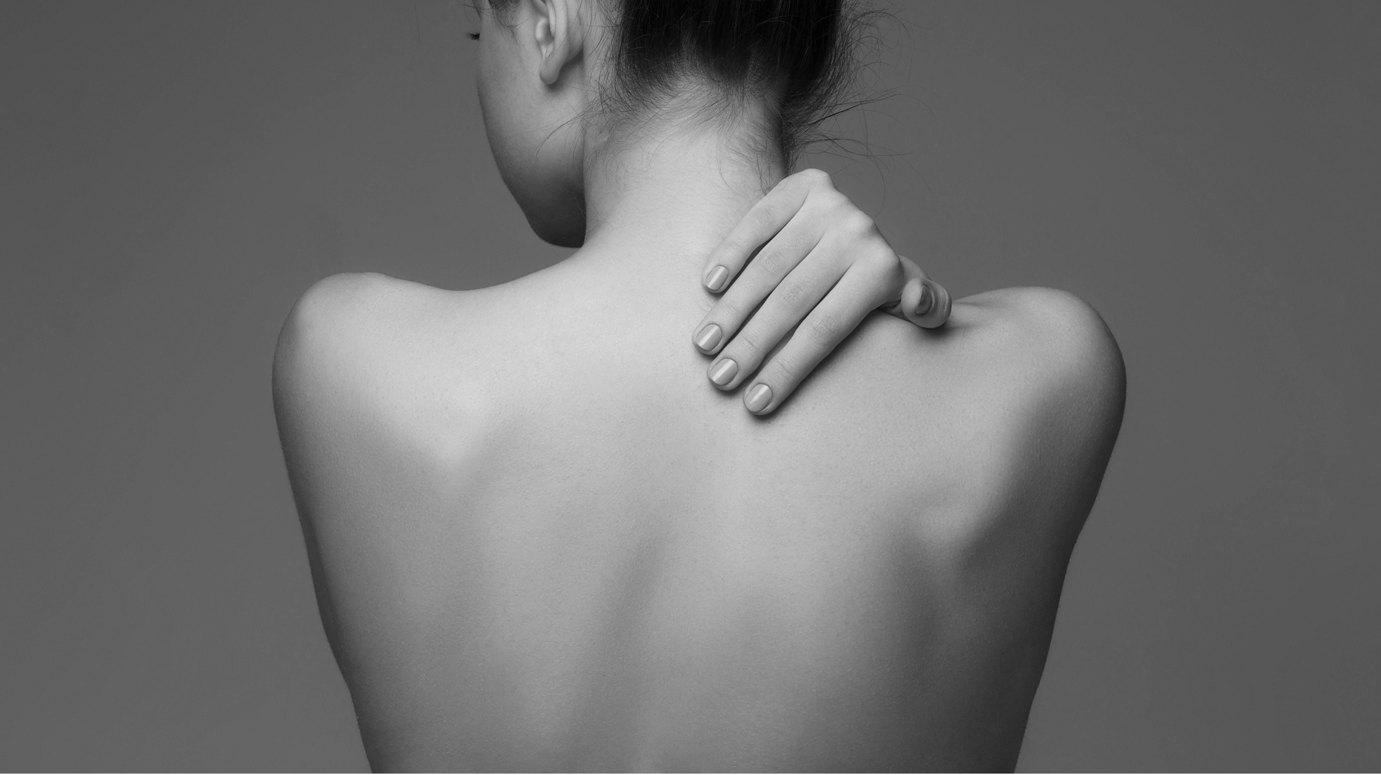 Rückansicht einer Frau mit freiem Rücken, die mit der rechten Hand ihren Nacken hält.