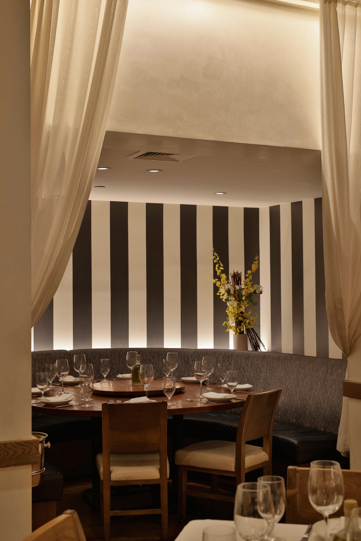 A modern restaurant interior featuring wooden tables, soft lighting, and elegant curtains draping from the ceiling.
