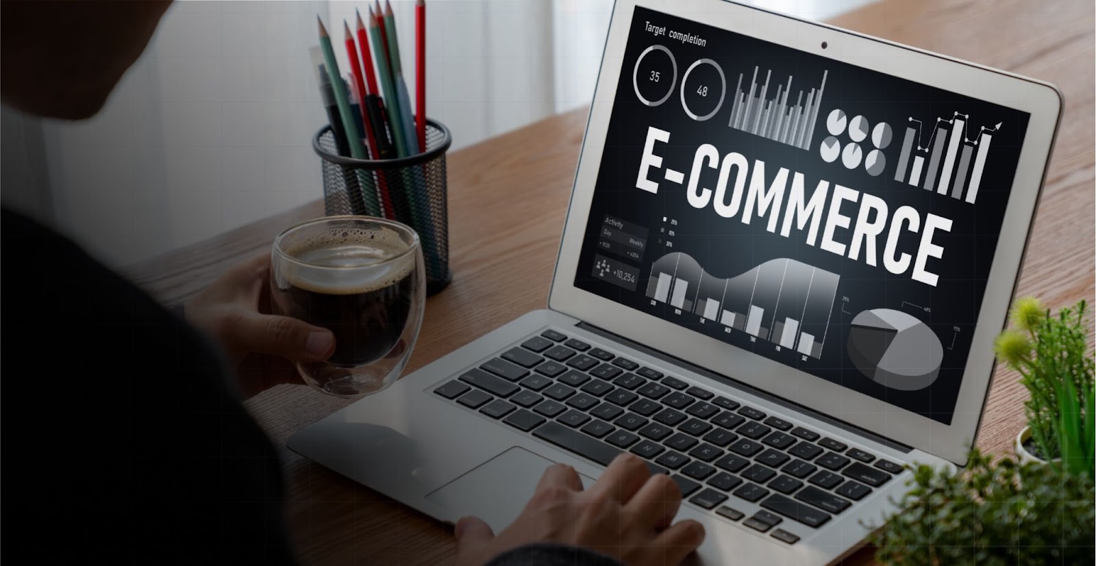 Person mit Kaffee am Laptop mit einem E-Commerce-Dashboard voller Diagramme
