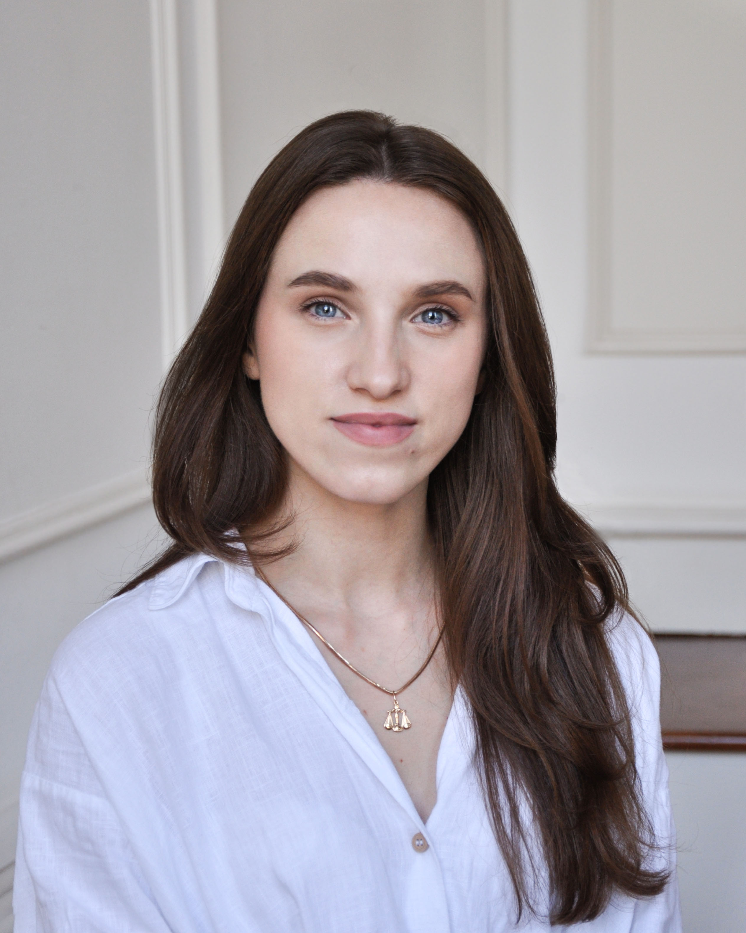 Portrait of Yuliia, a helpline operator at Empatia by OPORA, wearing a white blouse and smiling softly.