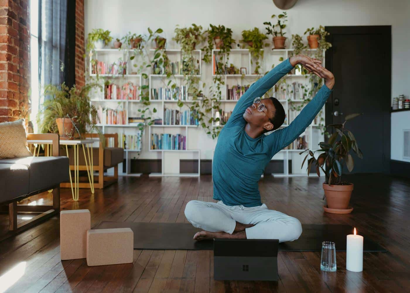 Man sitting on yoga mat at home stretching his arms above his head