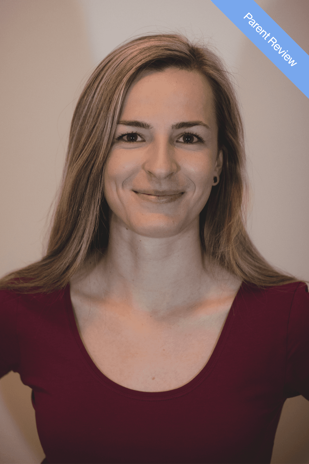 Man wearing an olive green jacket and black shirt, sitting and smiling in front of a light wooden background.