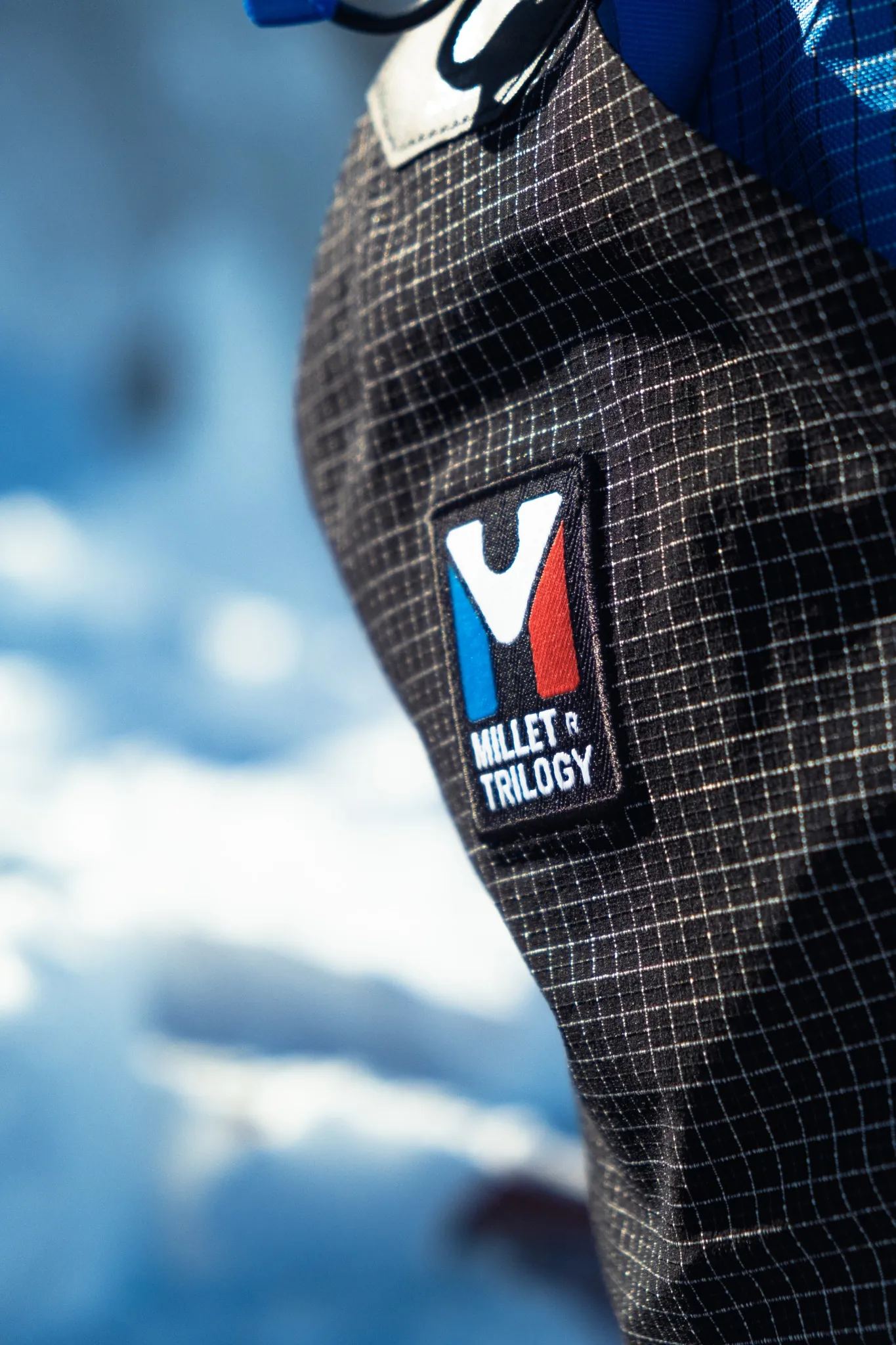 Détail du patch Millet Trilogy sur pantalon technique en montagne enneigée.