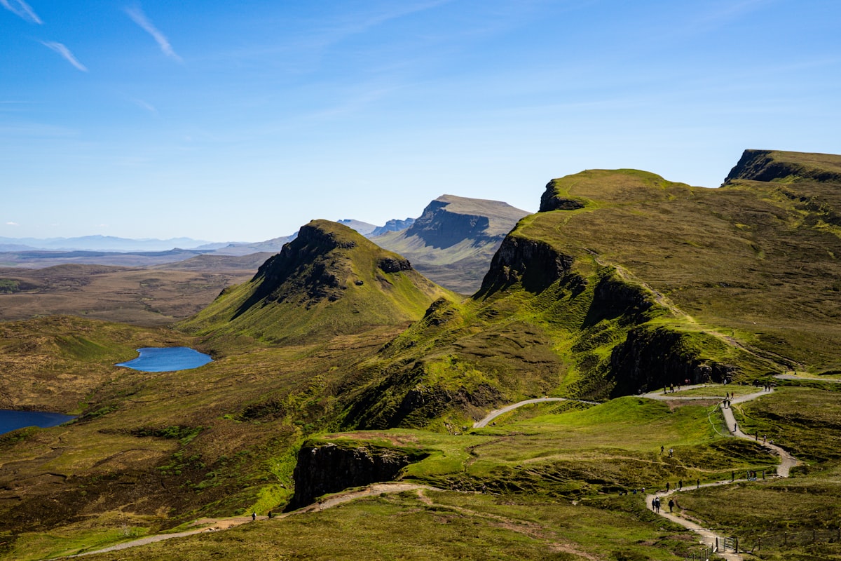 Rolling green hills with a winding path and distant lochs in the Scottish Highlands