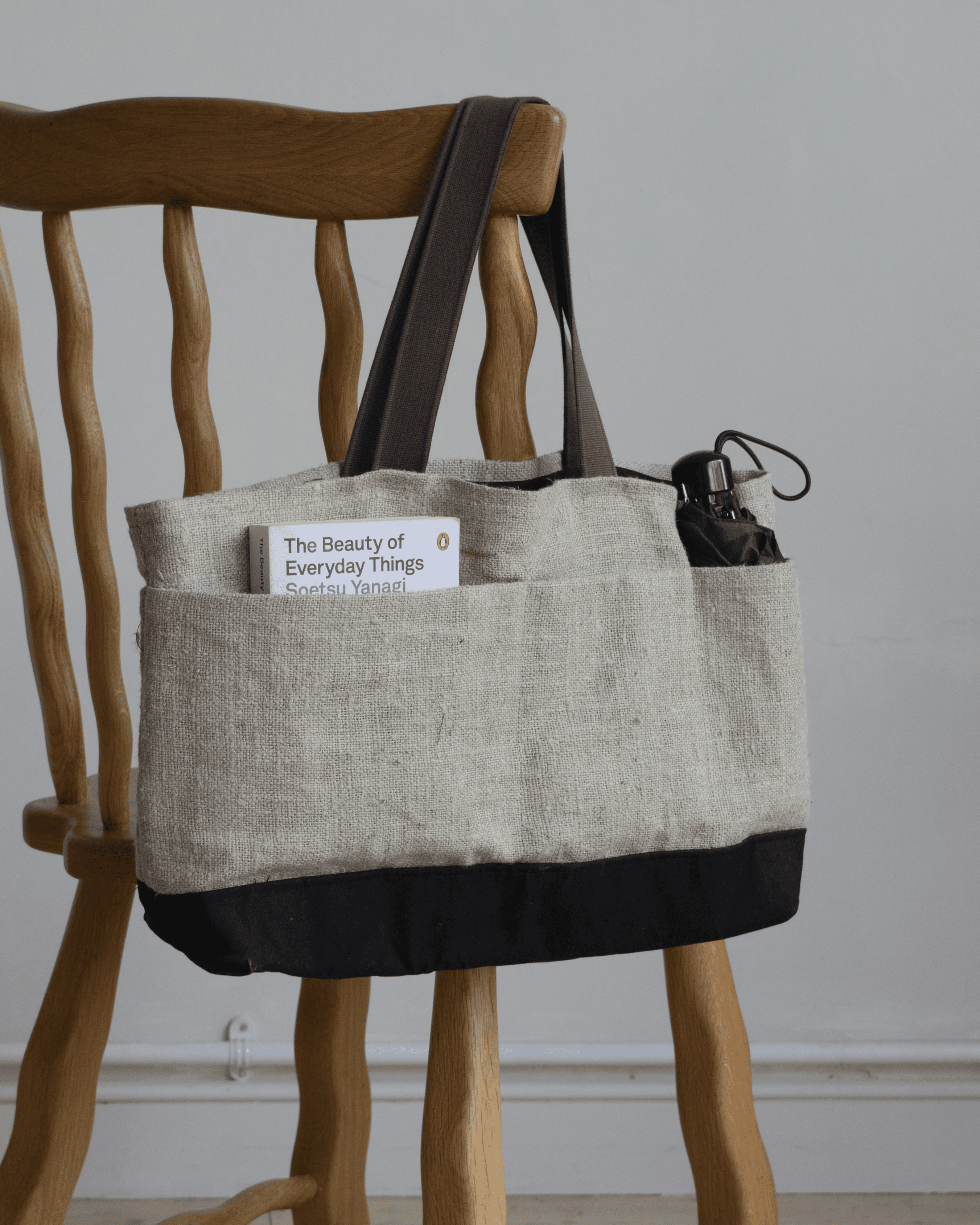 Limited edition Garden Tote from Wilkinson & Rivera in Raw Linen hanging from chair with book in one pocket and umbrella in another