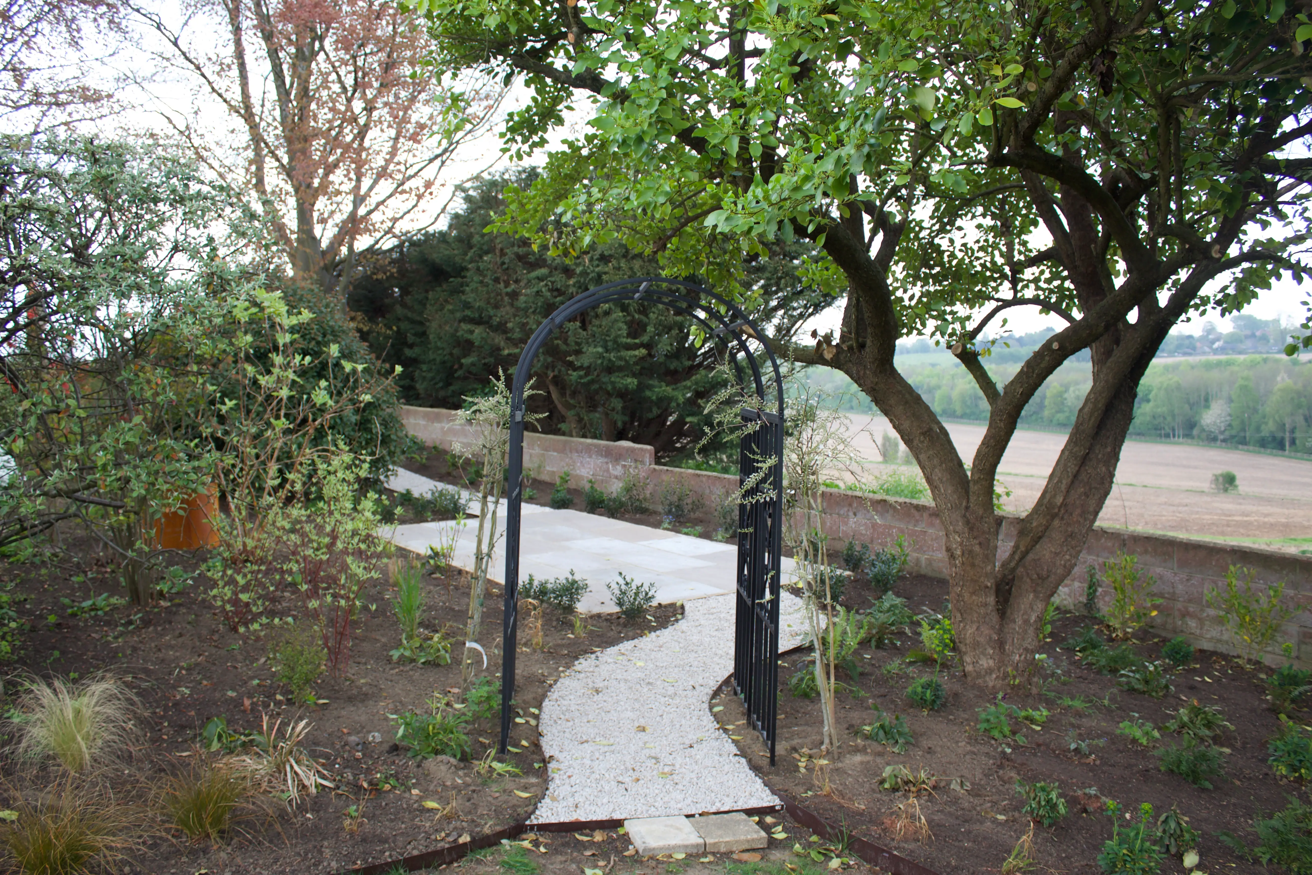 A serene garden path winds through greenery, flanked by trees and plants, leading into a tranquil outdoor space.