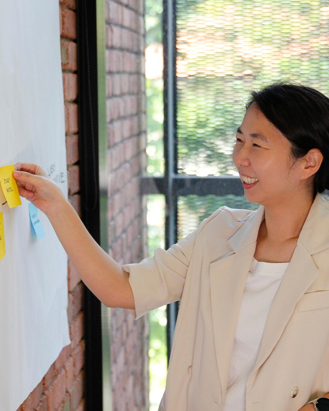 A side profile image of our team member, Hye Yoon, who's sticking a yellow post-it note on the whiteboard.